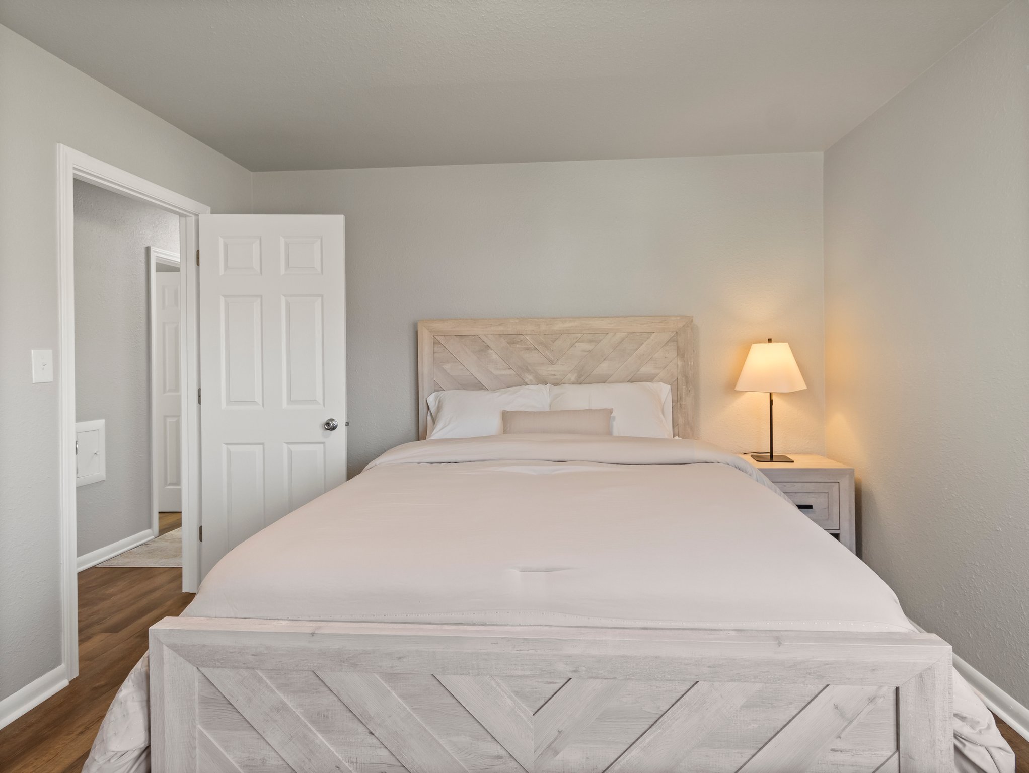 Boutique, guest‑ready bedroom with white bedding, a wooden dresser and mirror, bay‑window natural light, and a calm, curated hospitality aesthetic.