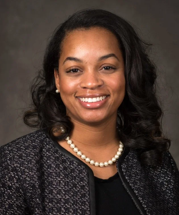 Professional portrait of a woman in neutral attire, smiling against a soft gray background.
