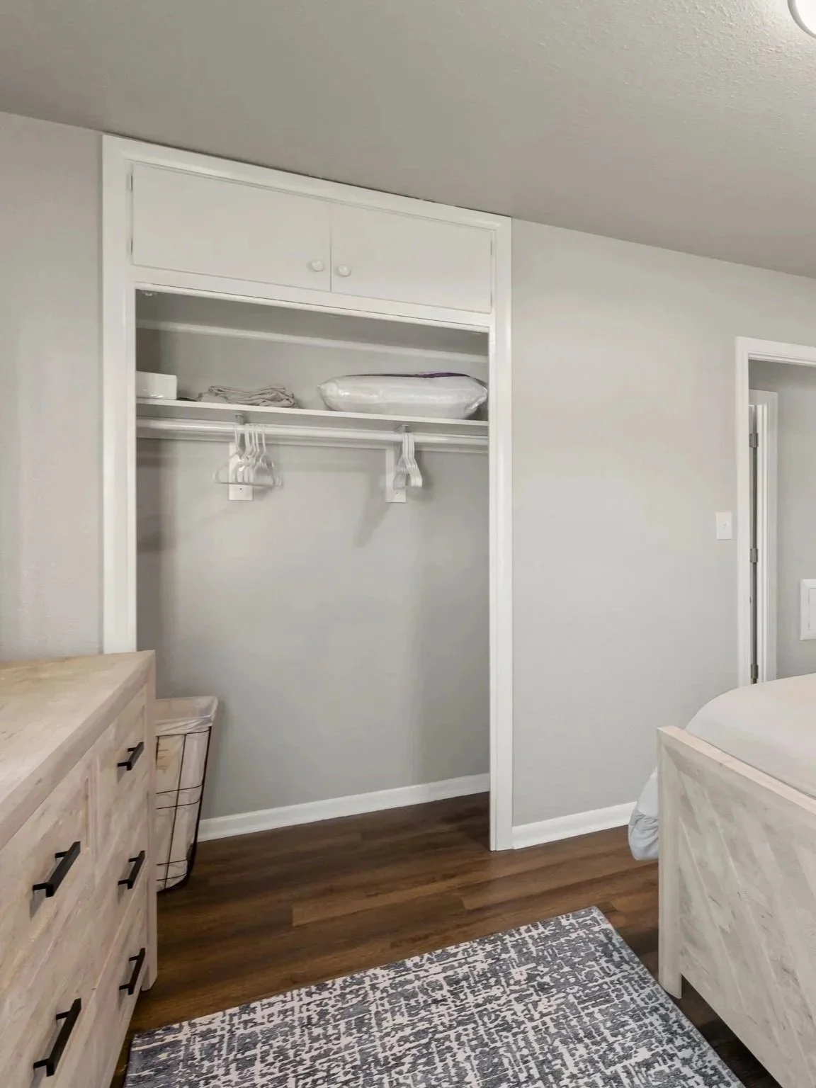 Boutique, guest‑ready bedroom with white bedding, a wooden dresser and mirror, bay‑window natural light, and a calm, curated hospitality aesthetic.