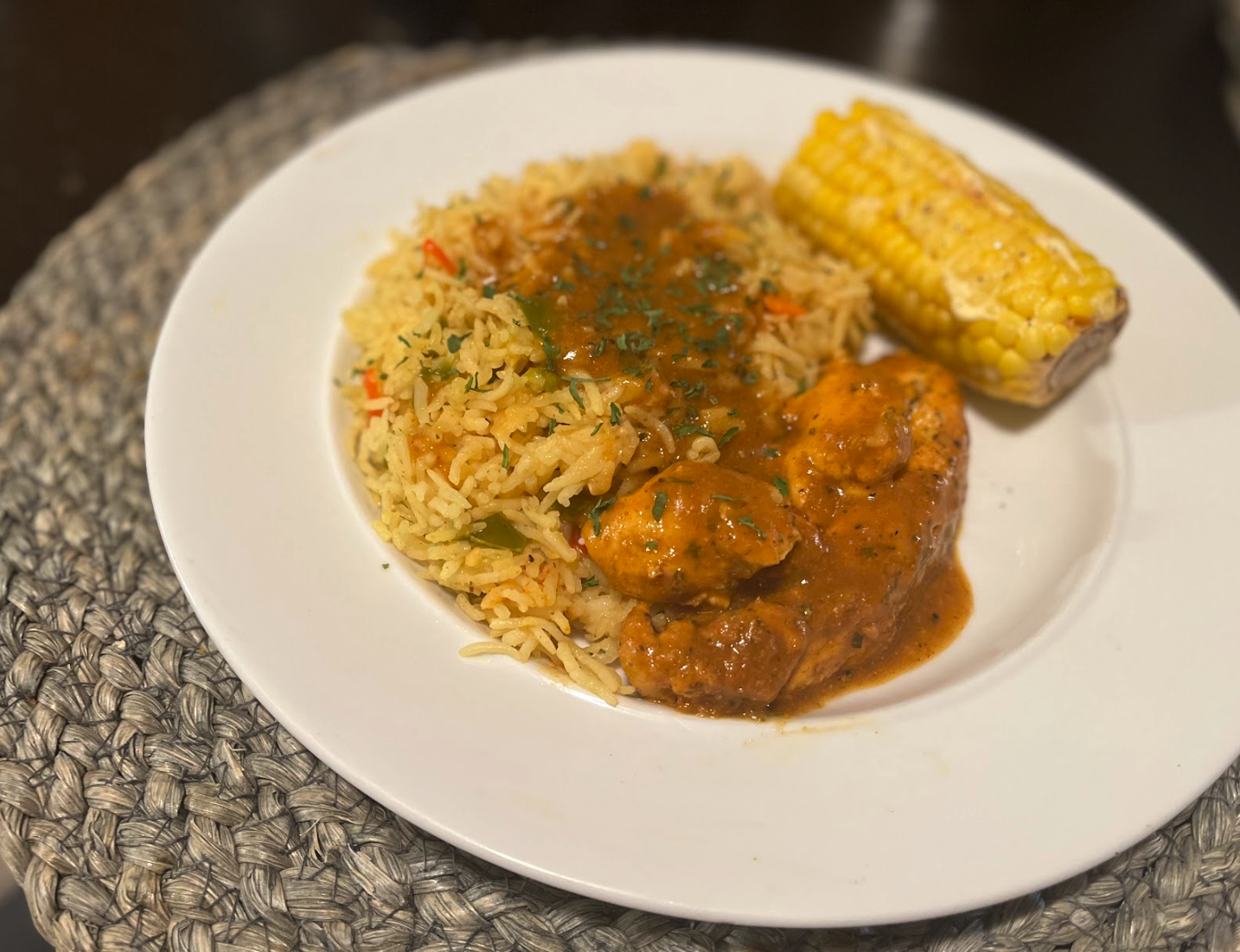Plate of rice with vegetables, a serving of chicken in sauce, and grilled corn on the cob.