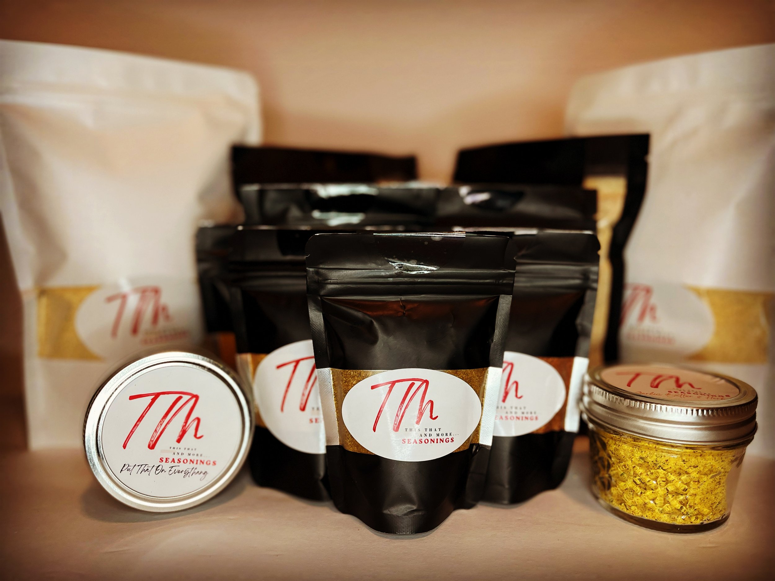 Assorted seasoning jars and pouches with labels from Th. The collection includes four resealable black pouches, two larger white bags, a small metal tin, and a glass jar with yellow seasoning flakes.