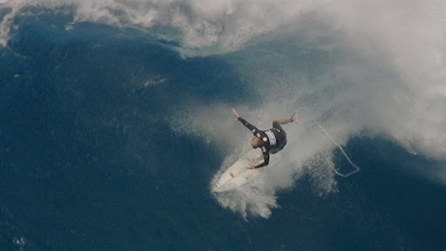 A surfer riding a large wave, leaning into the wave with the surfboard tilted on its side.