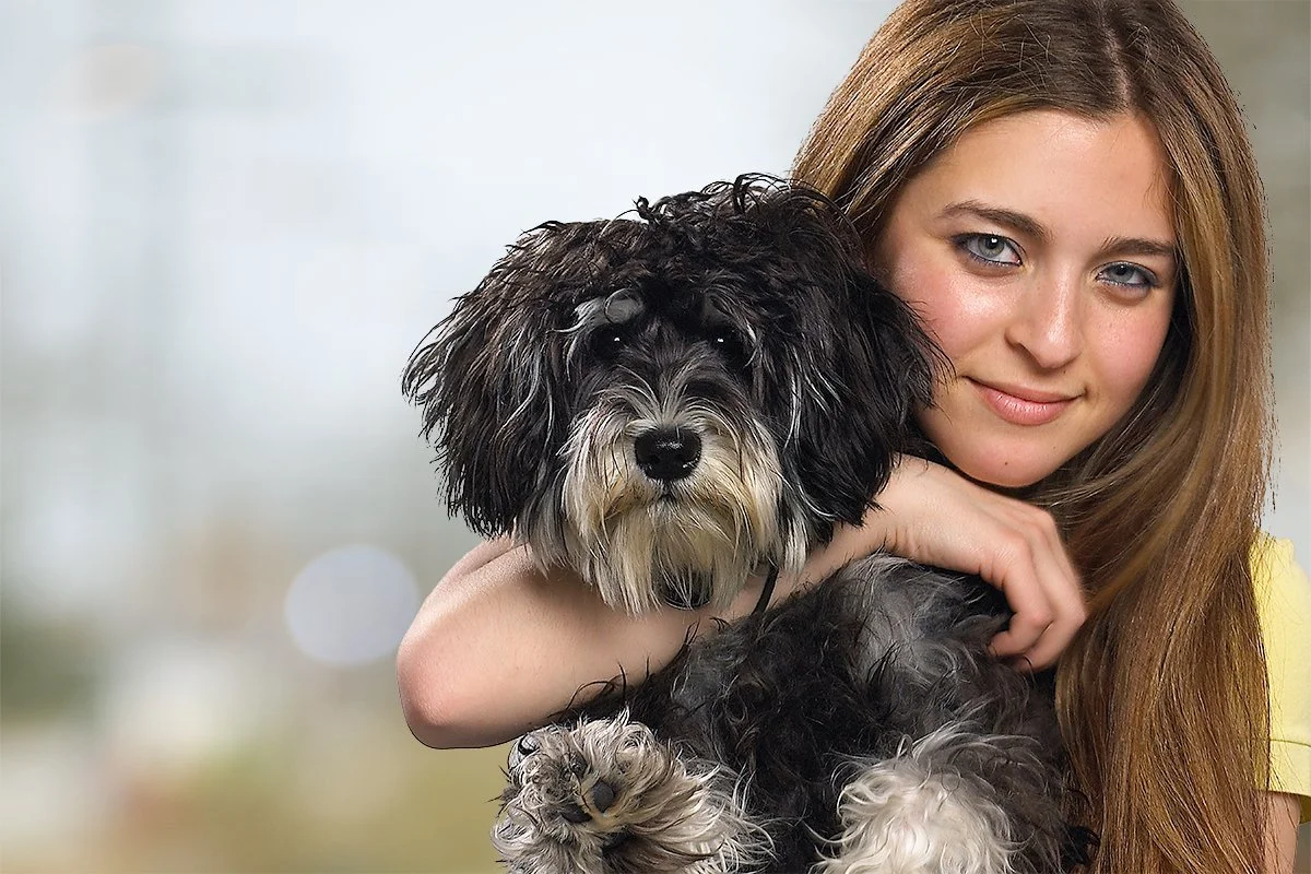 A young woman with long reddish hair hugging a black and white dog with curly fur