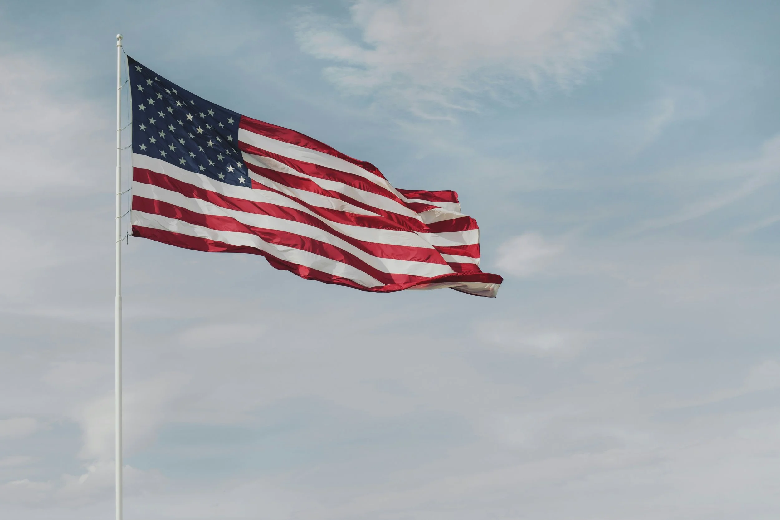U.S. flag waving in the wind against a cloudy sky.