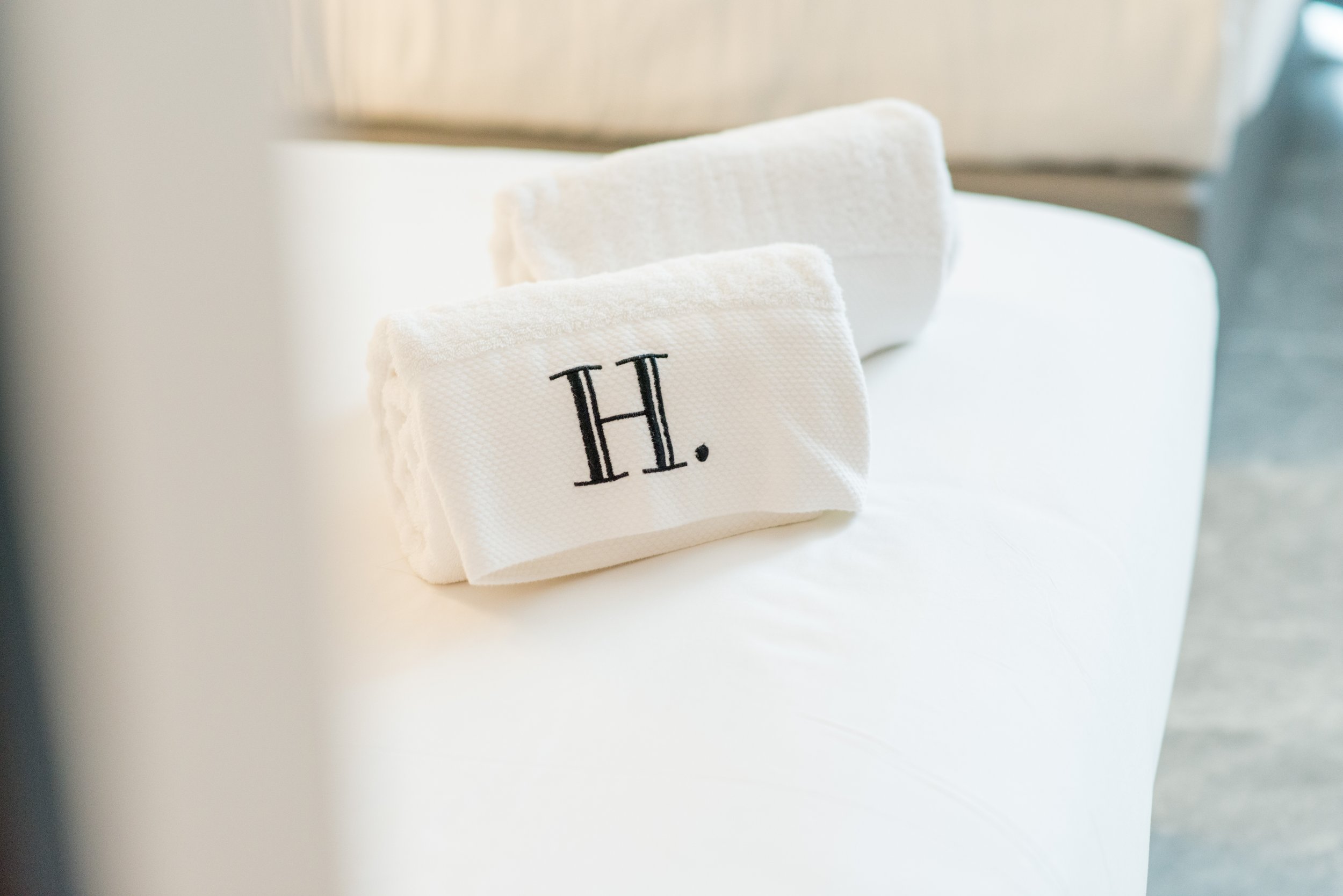 A set of white towels with the initials 'H.' embroidered on the front, placed on a white surface.