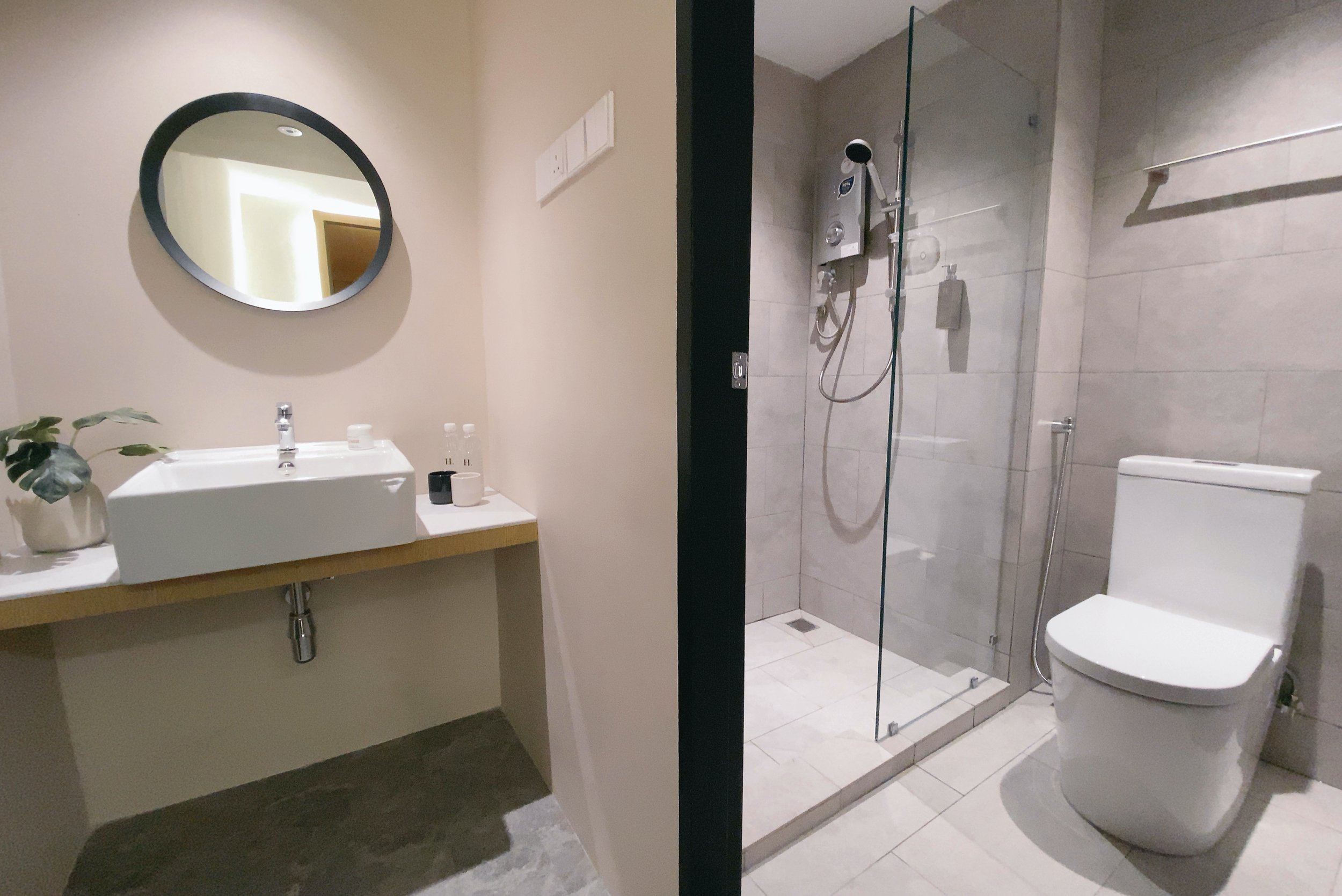 A split view of a modern bathroom with a sink and mirror on the left, and a shower and toilet on the right.
