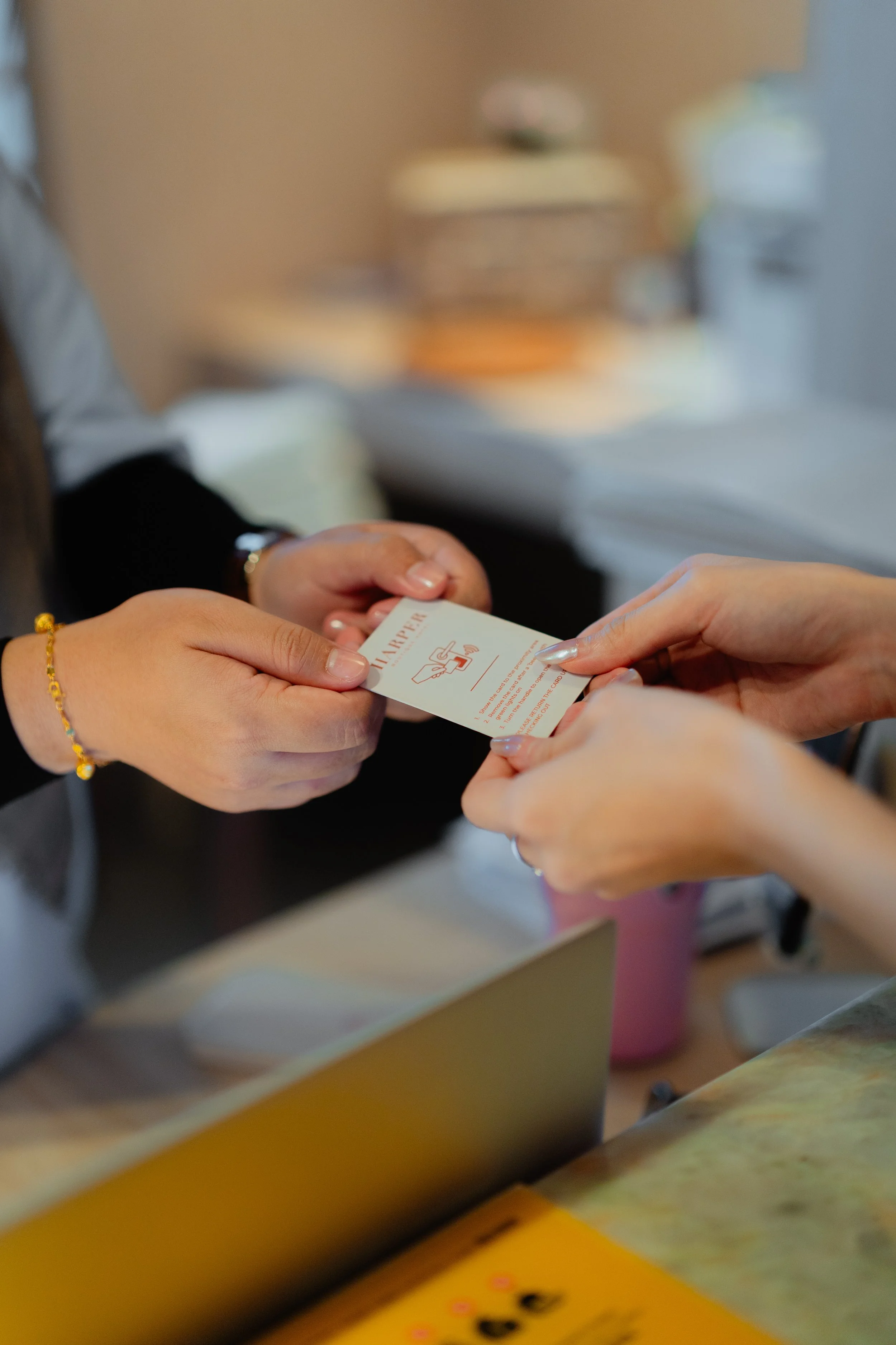 Two people exchanging a business card at a desk, with blurred background showing plates and furniture.
