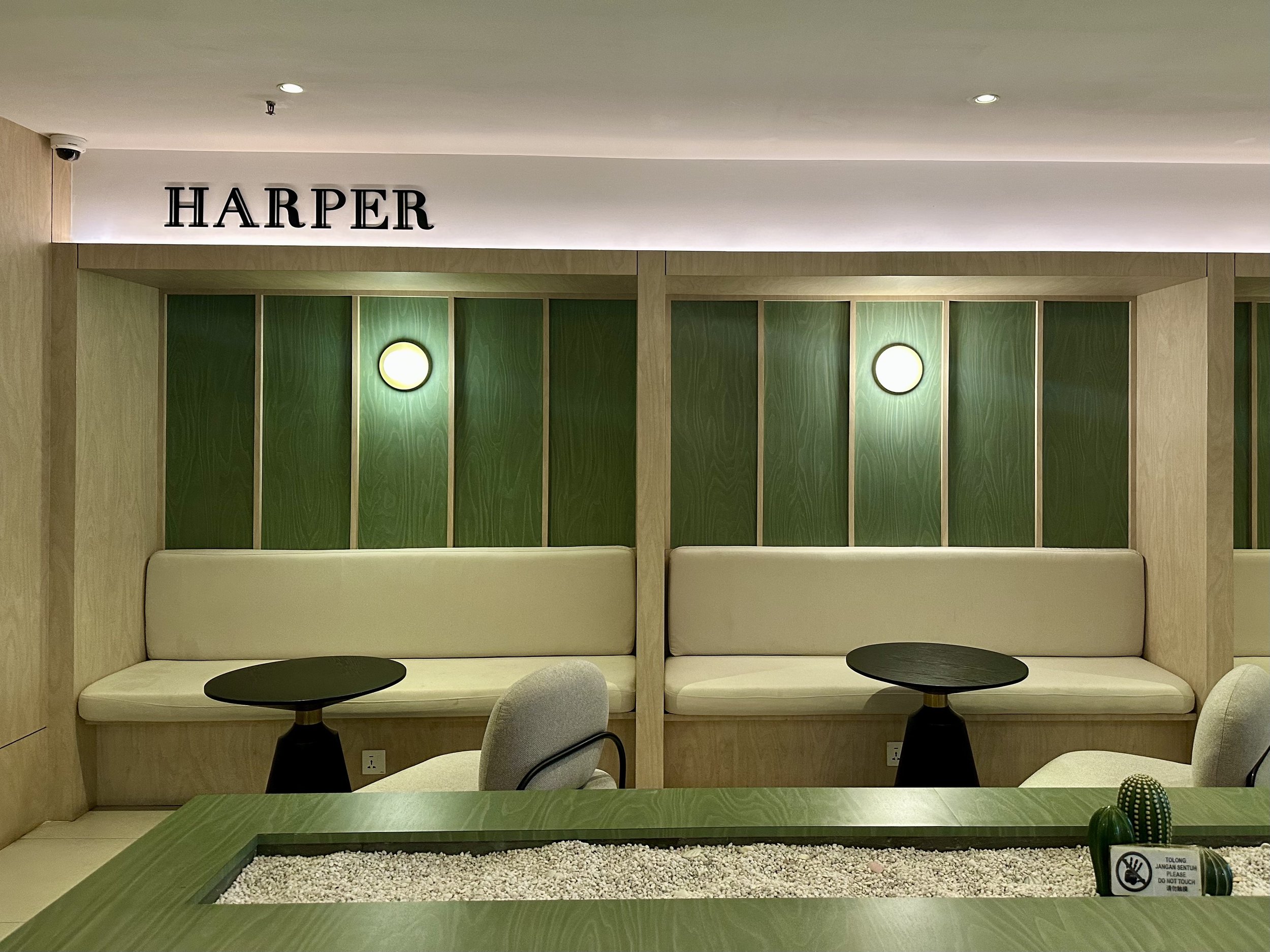 Interior seating area with beige cushioned benches, small black tables, and green wood-paneled wall with wall sconces. The sign 'Harper' is on the upper wall.