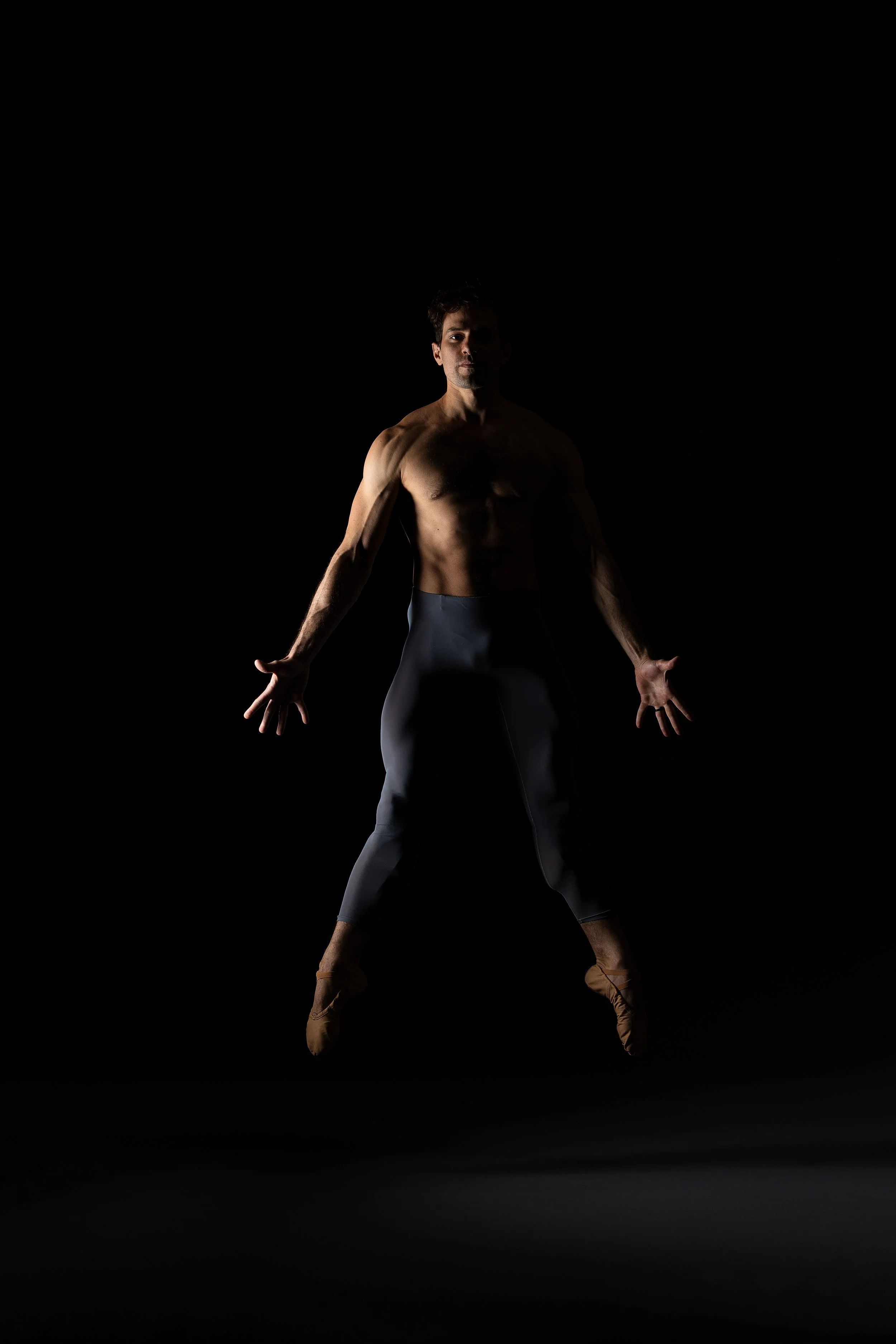 Ballet dancer mid-jump against a black background