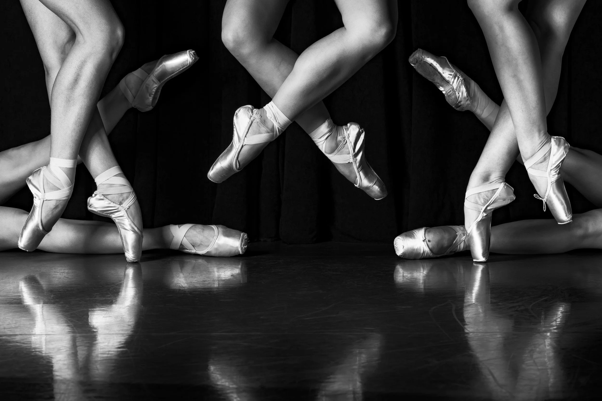 Black and white photo of ballet dancers' legs and feet, wearing pointe shoes, performing on stage.