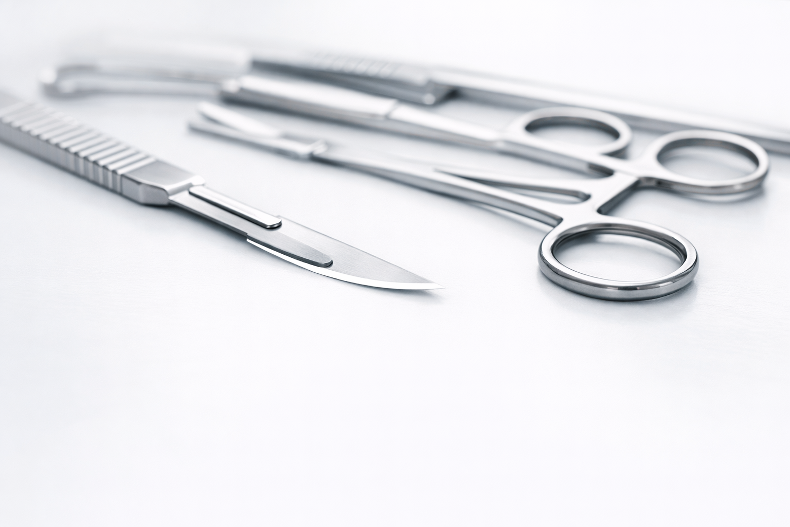 Set of surgical scissors and a surgical scalpel resting on a white surface