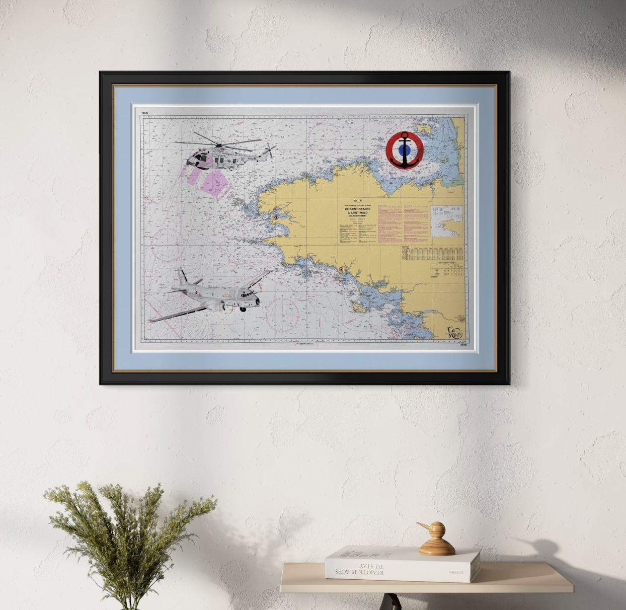 Carte maritime encadrée avec un logo d'ancre rouge et bleue, décorée d'illustrations d'hélicoptère et d'avion, suspendue à un mur blanc.