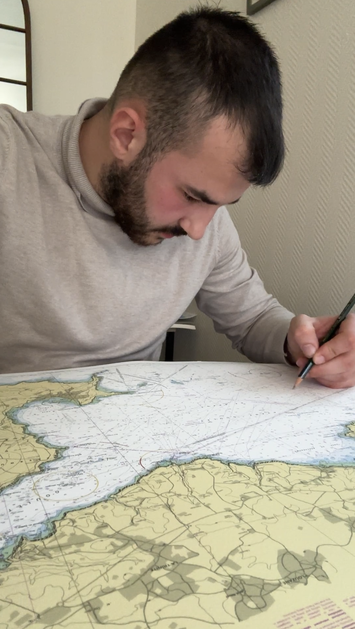Un homme regarde une carte maritime, probablement une carte nautique, et prend des notes avec un stylo.