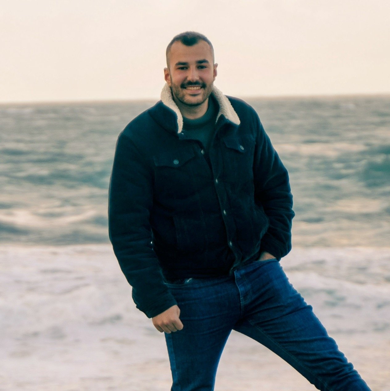 Un homme souriant debout sur la plage près de la mer par une journée venteuse.