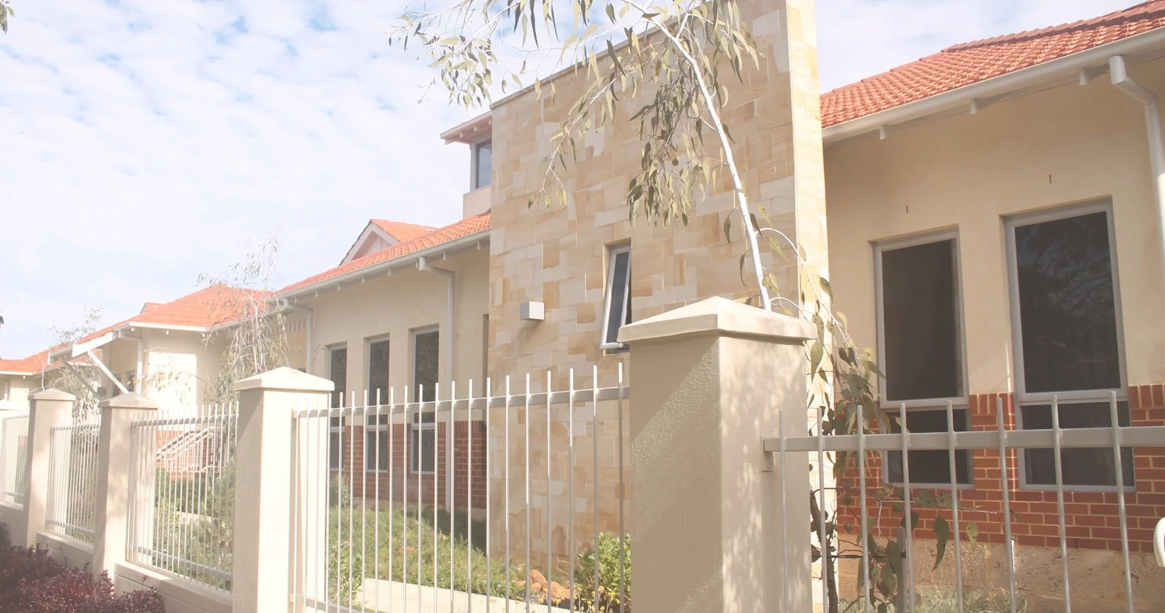 Project Management and Construction Servcies in Perth. Aged care redevelopment front view of modern multi-story residential building with beige walls, red tile roof, and a white metal fence.