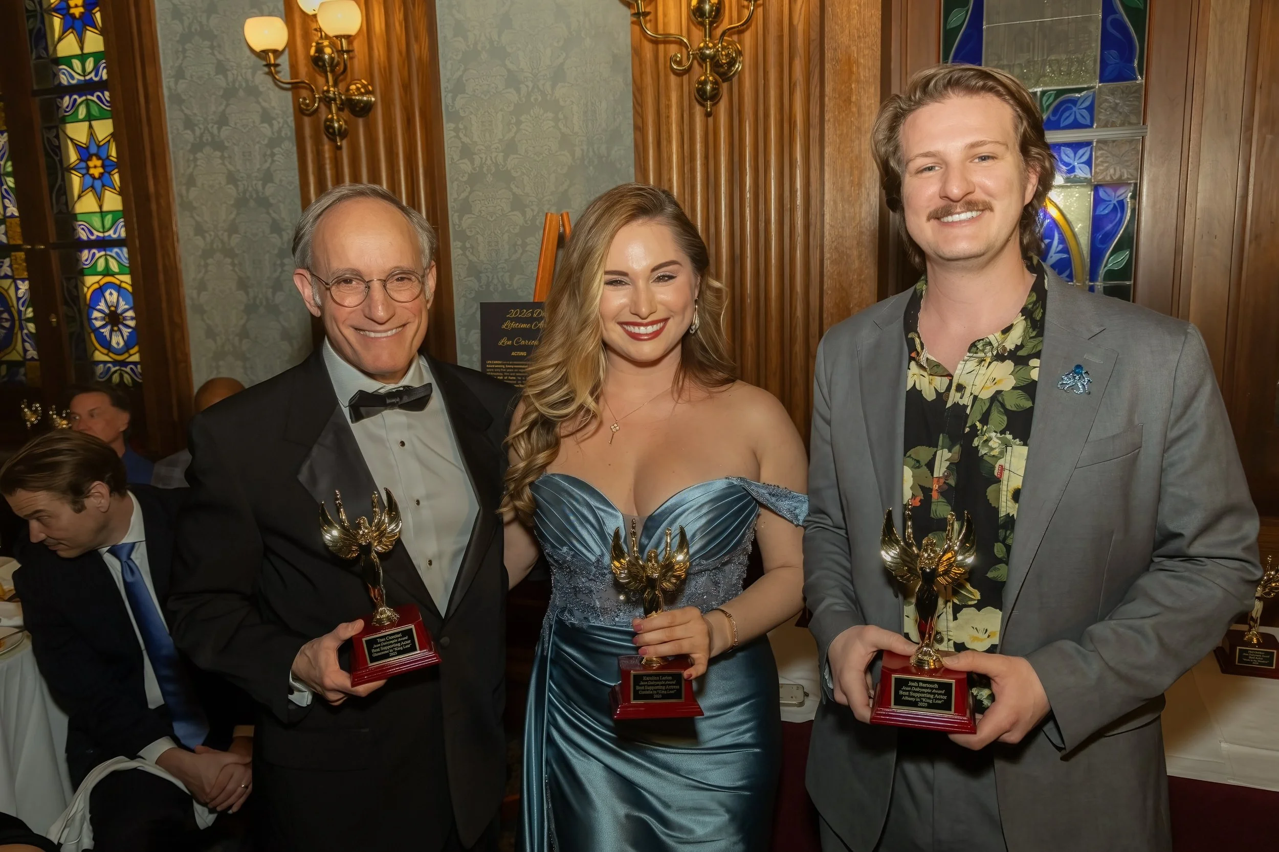 Group of three people with Karolina Larion at an award ceremony, holding trophies, dressed in formal and semi-formal attire, at the Penn Club in Manhattan.