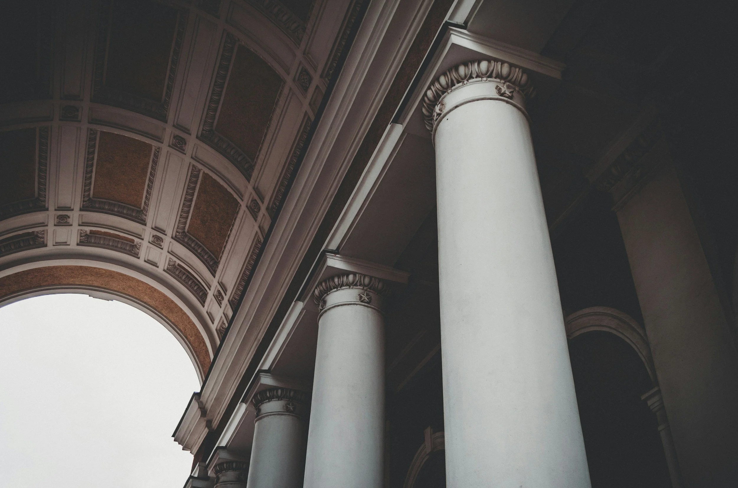 Three pillars of a structure with tall white columns and a decorated archway under a dark ceiling.