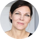 Close-up portrait of a woman with short dark hair and fair skin, wearing a black top, against a neutral background.