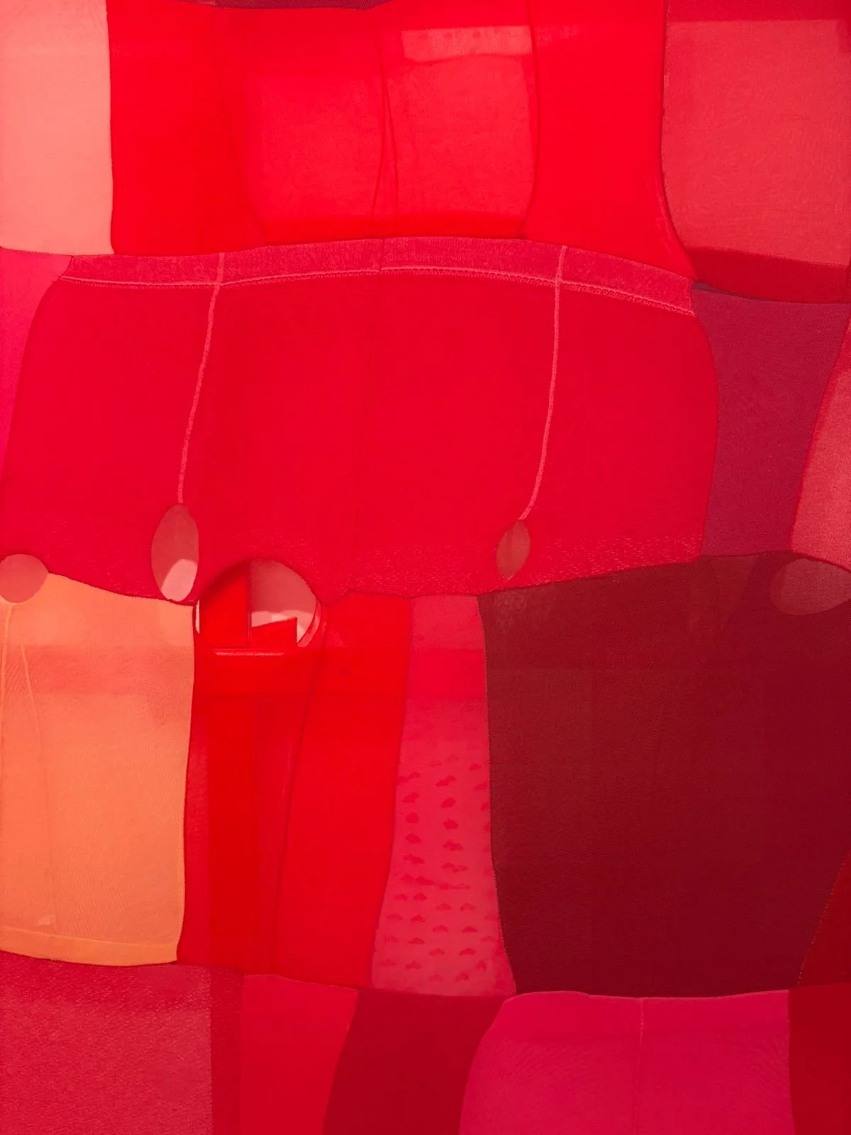 Close-up photo of a patchwork fabric with different shades of red and pink, featuring various textures and patterns.