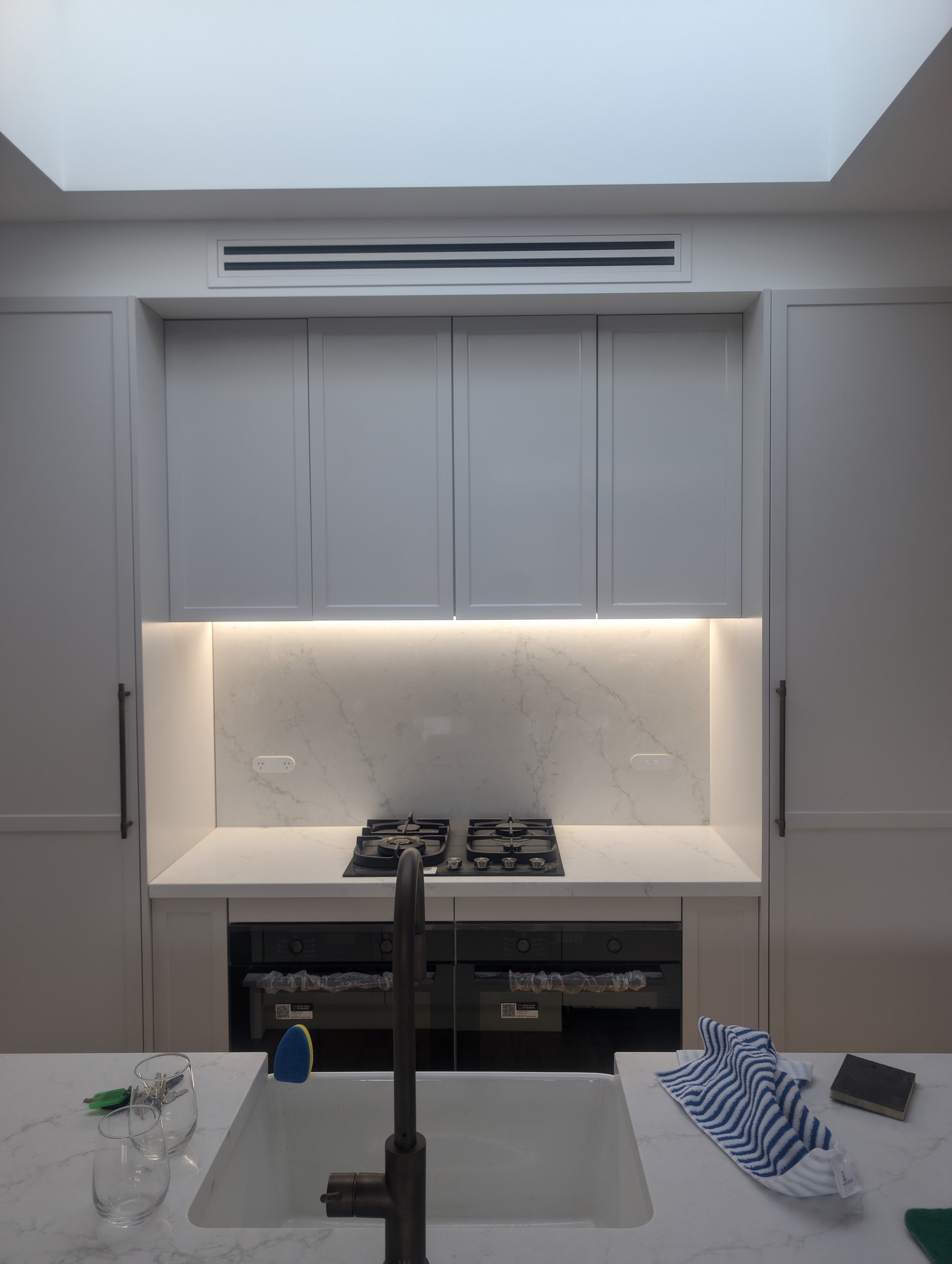 Modern kitchen with white cabinetry, a marble backsplash, a stovetop, and a sink with a faucet. A towel and a book are on the counter, with some glasses and a small object nearby.