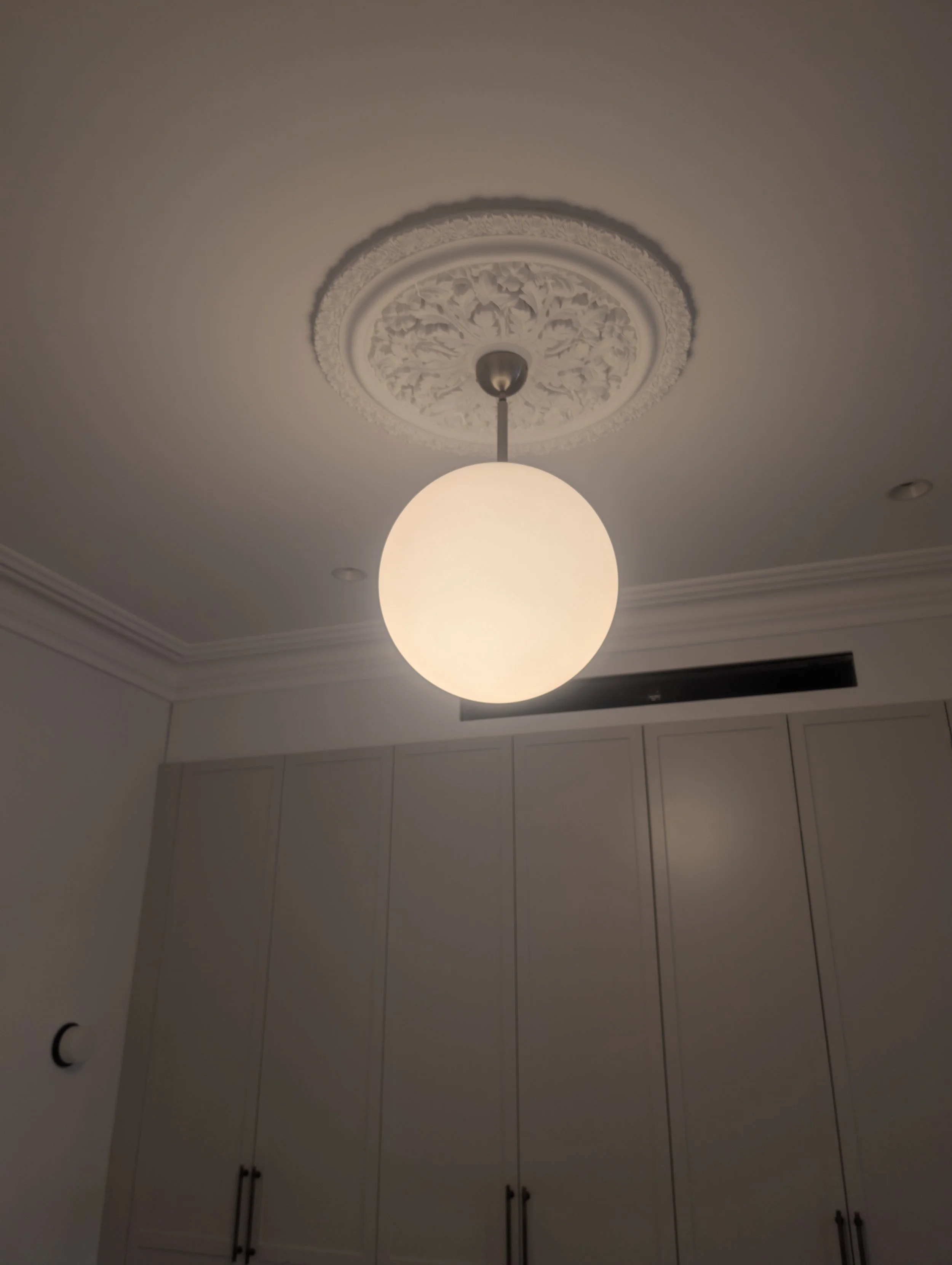 Ceiling light fixture with ornate decorative ceiling medallion in a room with cabinets.