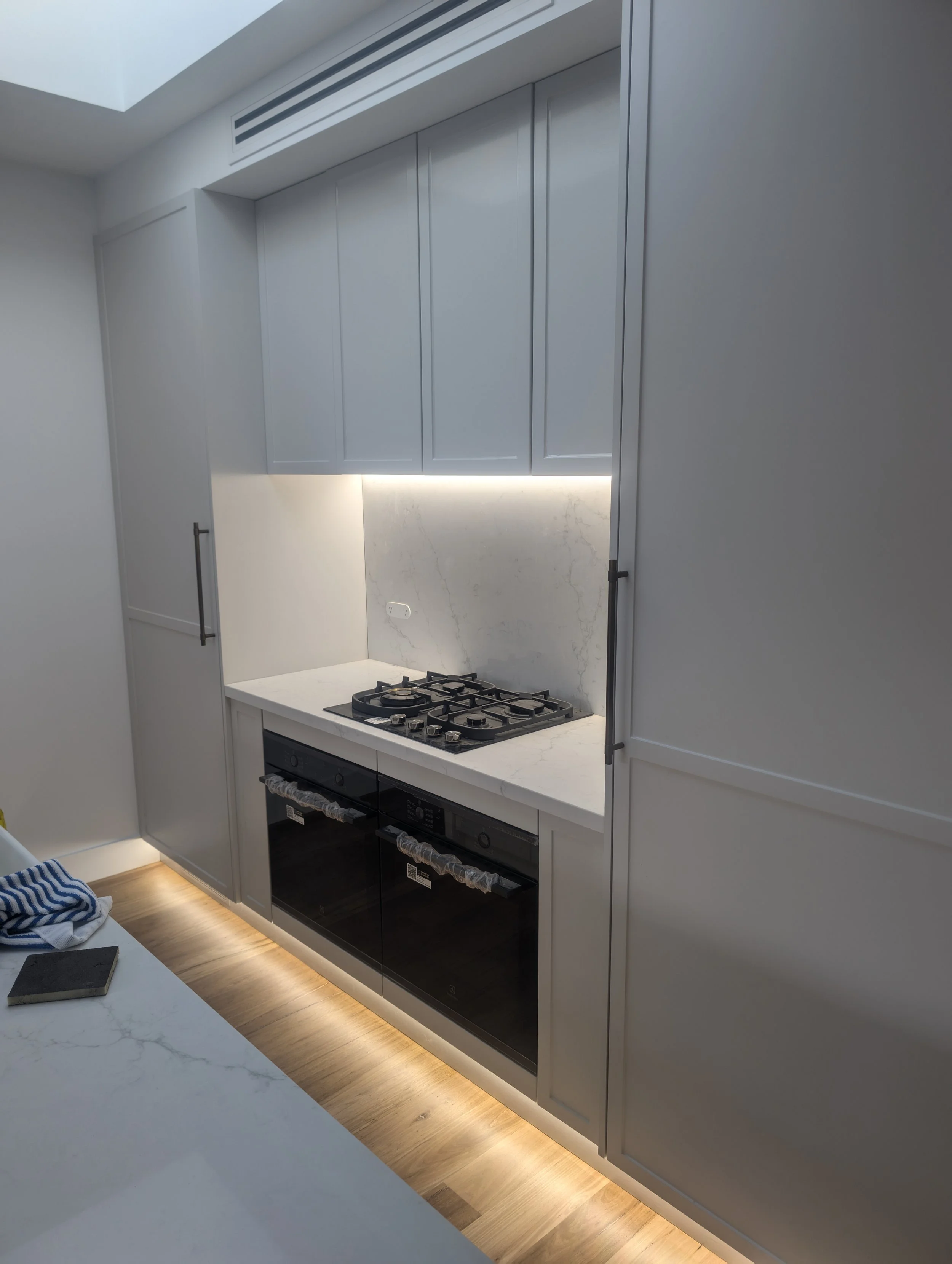 Modern kitchen with white cabinets, marble backsplash, built-in gas stove, and under-cabinet lighting. Part of a kitchen counter with a blue and white cloth.