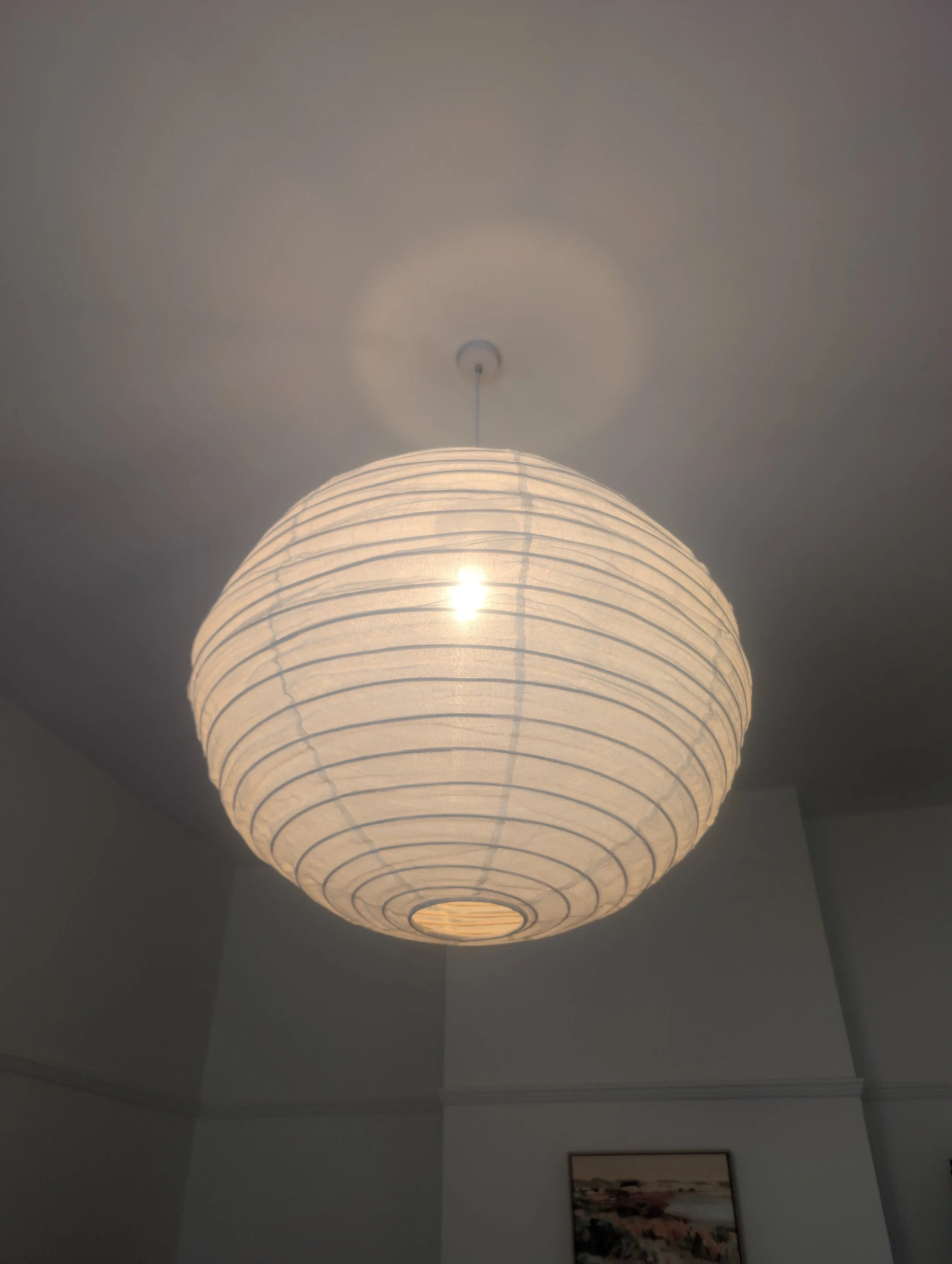 A hanging paper lantern light fixture in a room with a framed landscape picture on the wall.