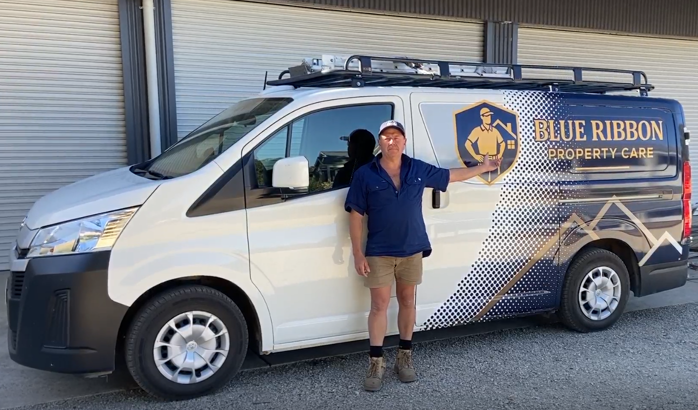 A man pointing at a company van with Blue Ribbon Property Care logo, standing in front of closed metal doors.