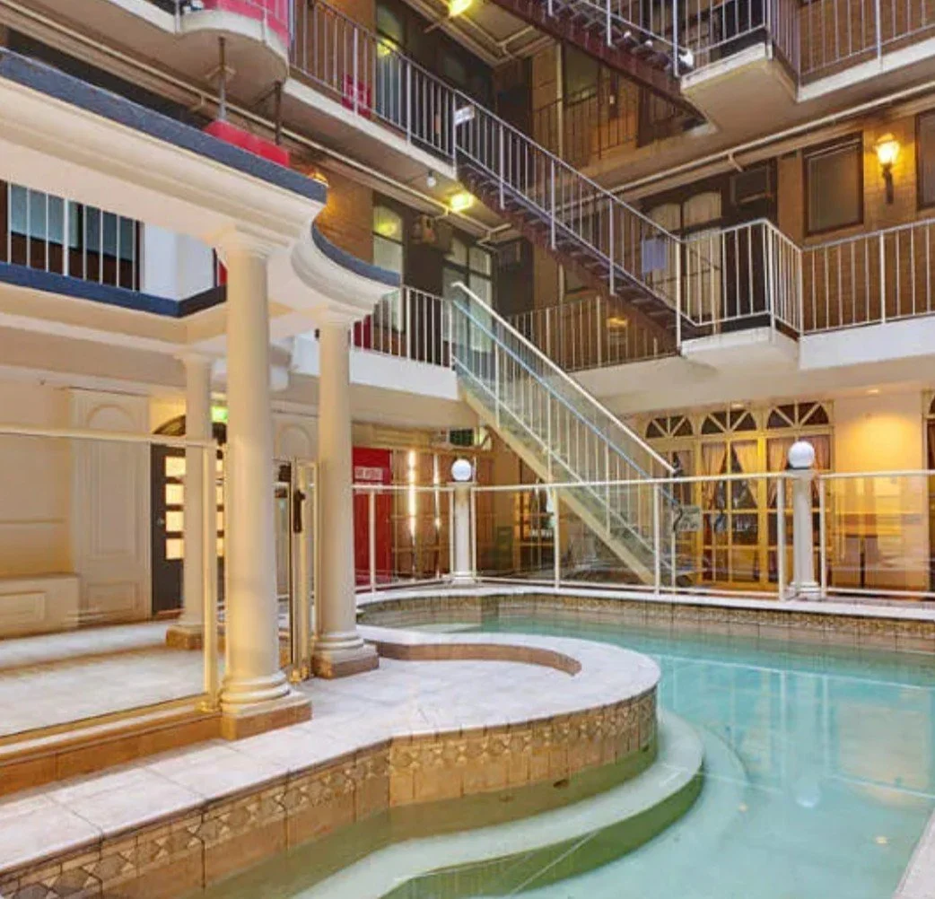 Indoor pool area with multi-level balconies, white pillars, and metal railings.