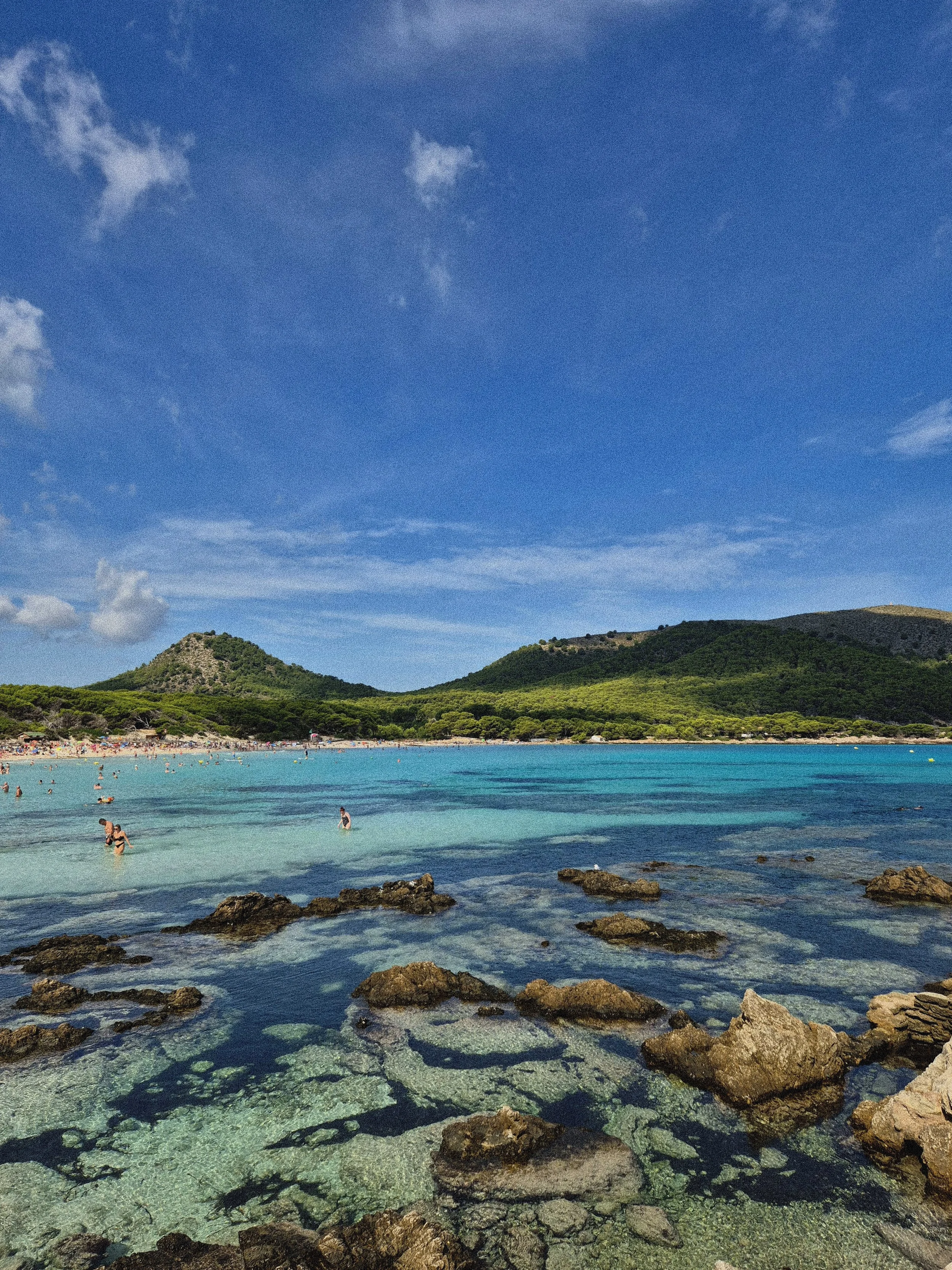 Beautiful beach with turquoise water, green hills on the background and blue sky. It is Cala Agulla in Mallorca.