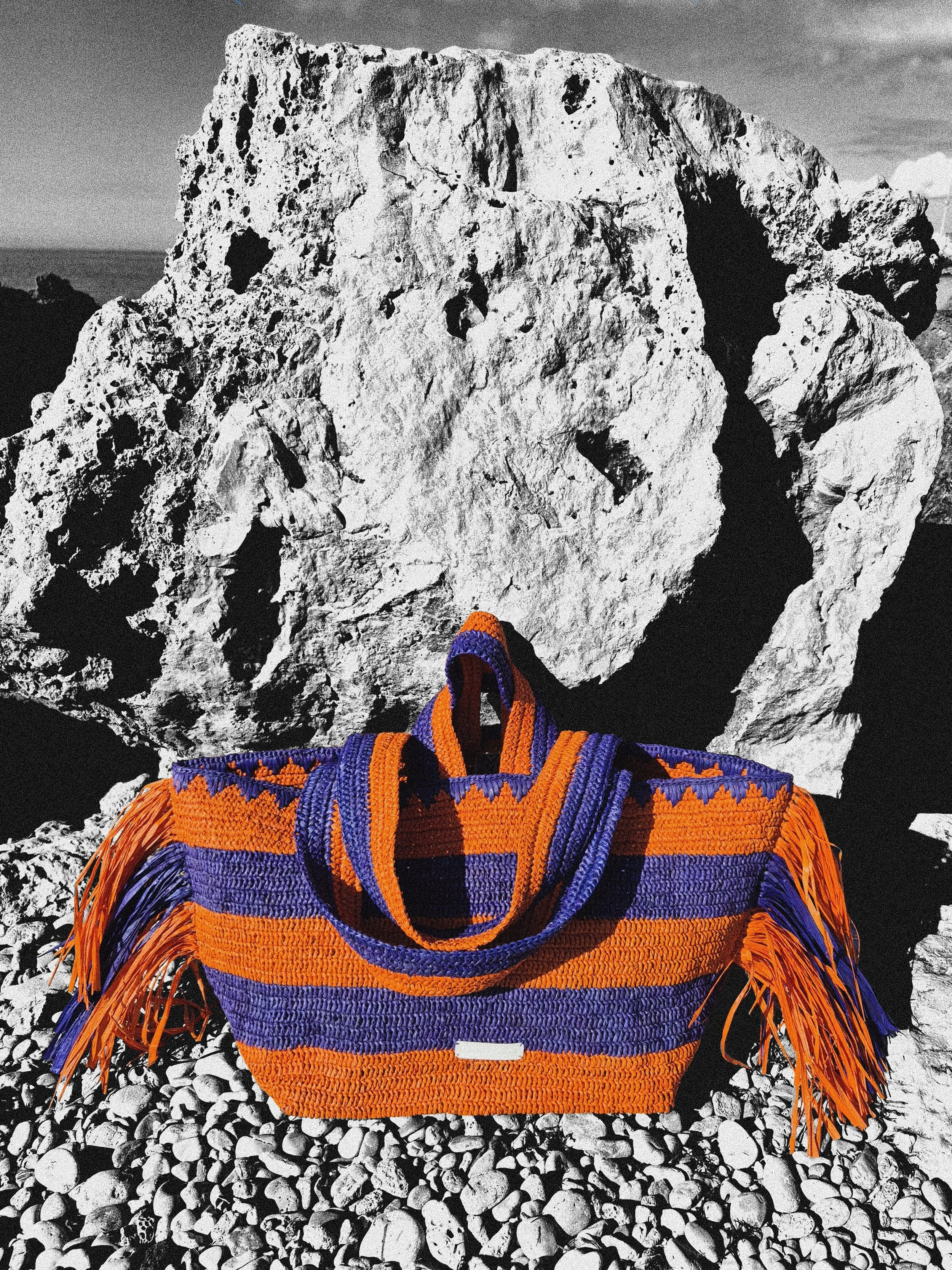 Packshot crochet bag in raffia Le Soller from the label 'KAMACKO' in orange and blue stripes and fringes.