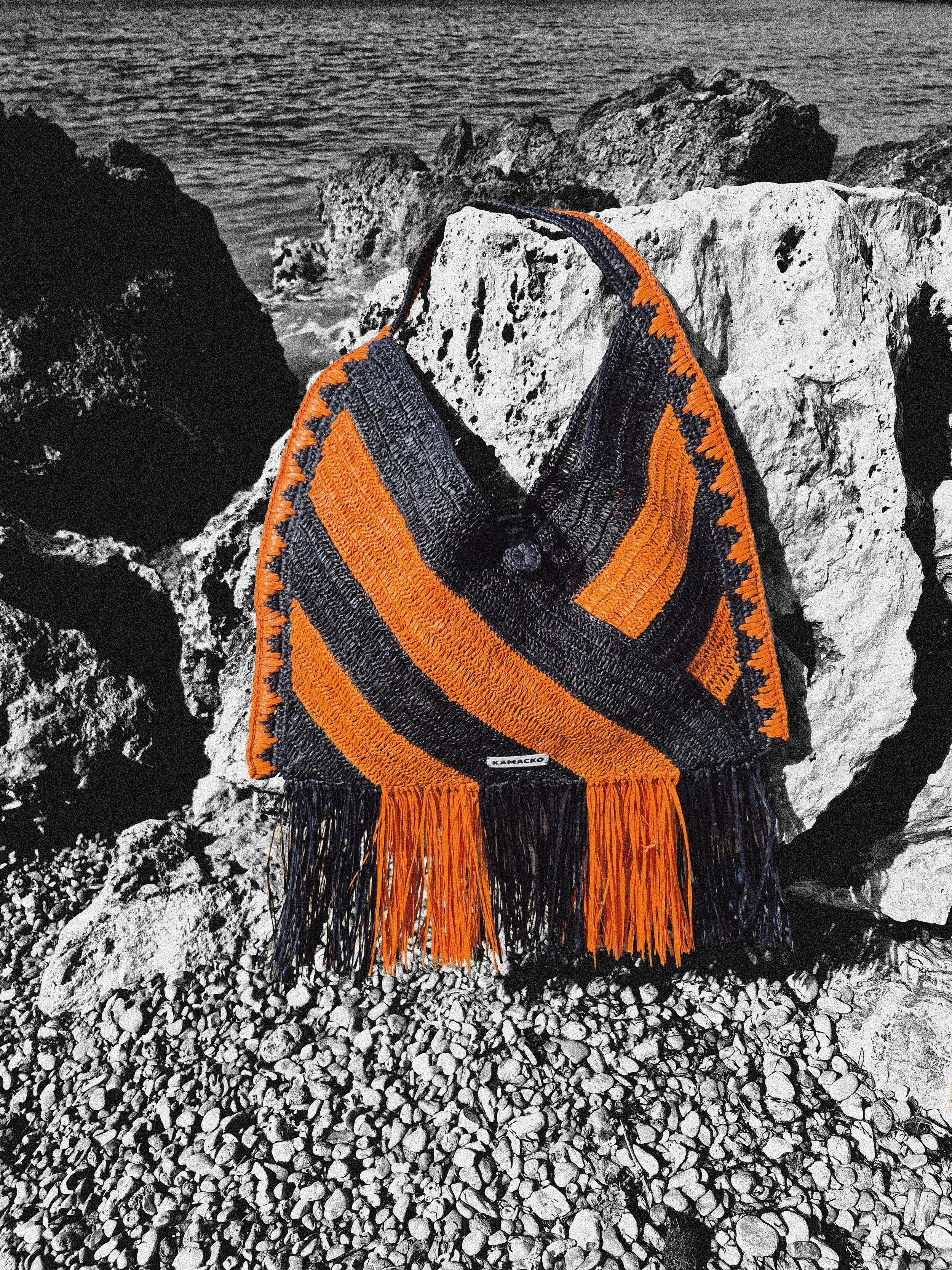 Packshot crochet bag in raffia Le Agulla from the label 'KAMACKO' in black and orange stripes and fringes.