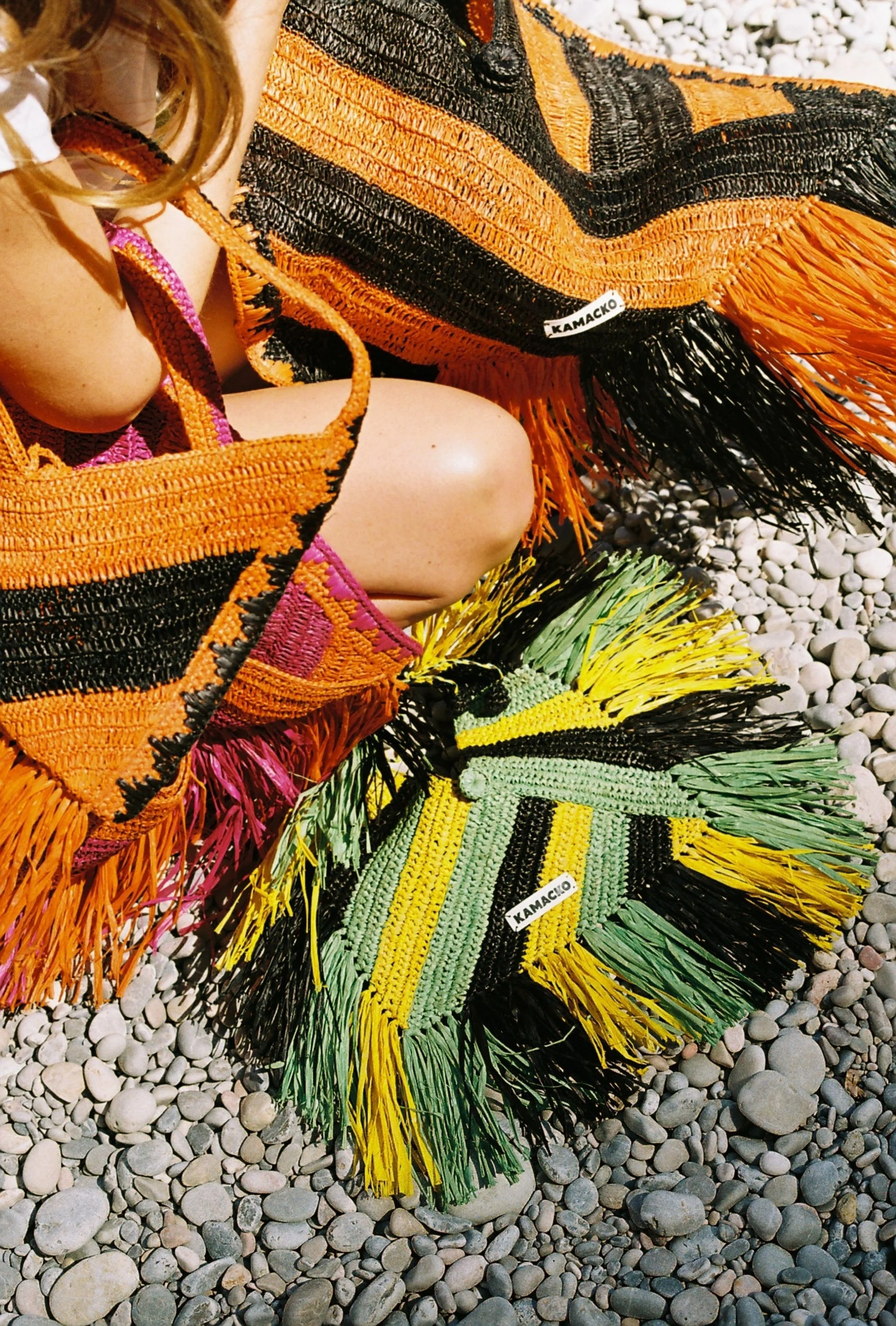 close up of a woman holding multiple handmade crochet bags from the brand Kamacko. The bags are colourful with stripes, you can clearly see the label "Kamacko".