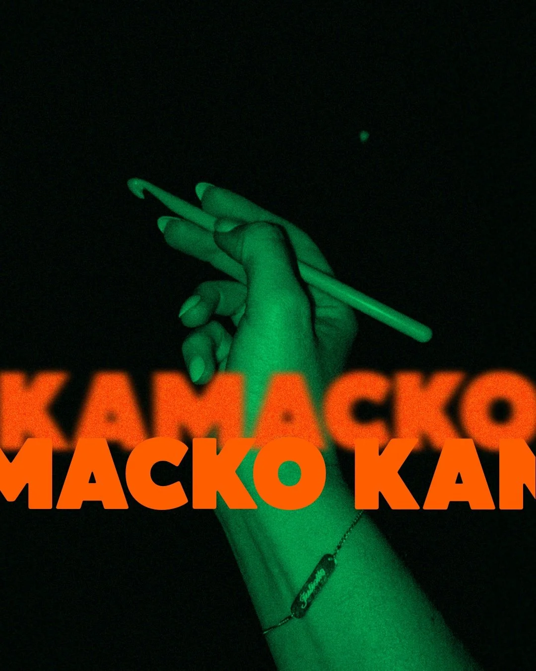 Hand holding a crochet hook. Hand highlited in green on a black background. On the foreground you can see the logo “KAMACKO" in orange.