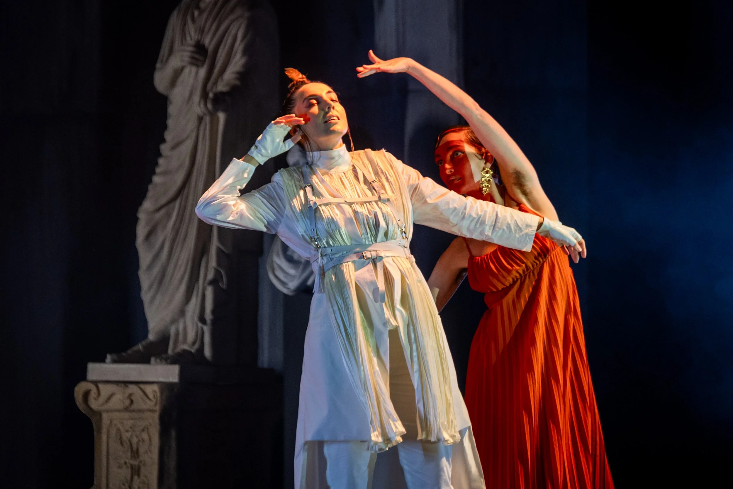 Two performers in contrasting white and red costumes move in a stylised duet before classical statues in Abos’ Pelopida, directed by Brett Nicholas Brown