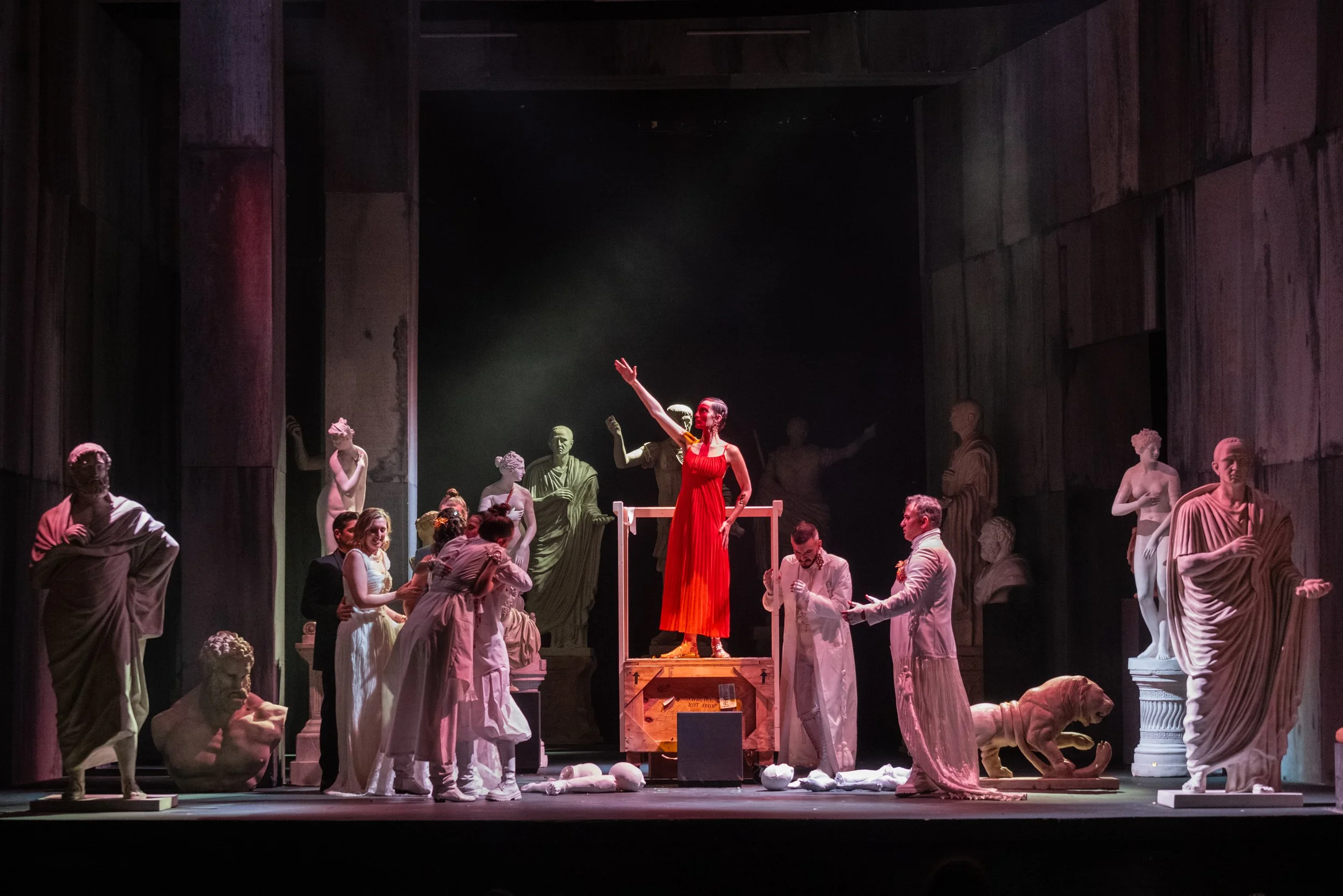 Scene from Girolamo Abos’ Pelopida (1747) at the Valletta Baroque Festival, directed by Brett Nicholas Brown, featuring a central female figure in a red dress surrounded by performers among classical statues