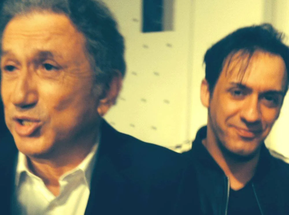 Deux hommes, l'un plus âgé à gauche et un plus jeune à droite, posent pour une photo.