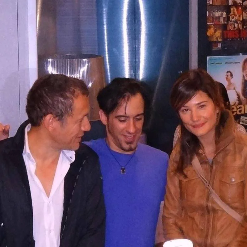 Trois personnes posant pour une photo dans un lieu intérieur avec affiches au mur. 