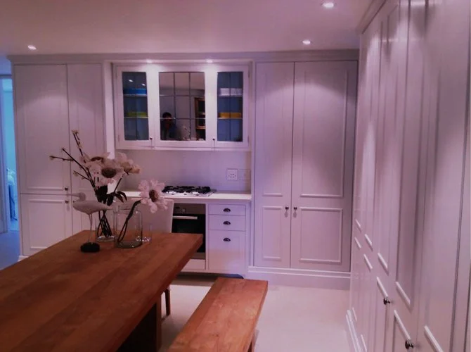 White kitchen with wooden dining table, flowers, and built-in cabinets.