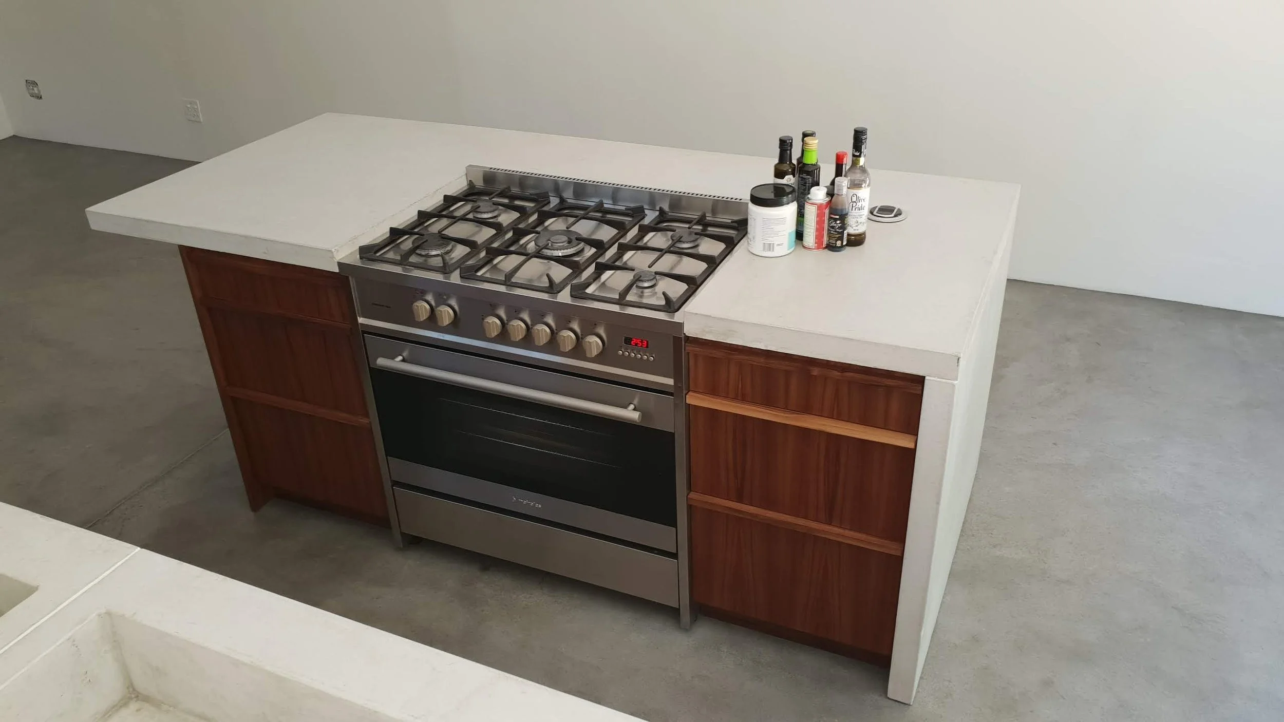 Kitchen stove with a white countertop, several bottles of condiments and spices on the right side, and a wooden cabinet with three open shelves underneath.