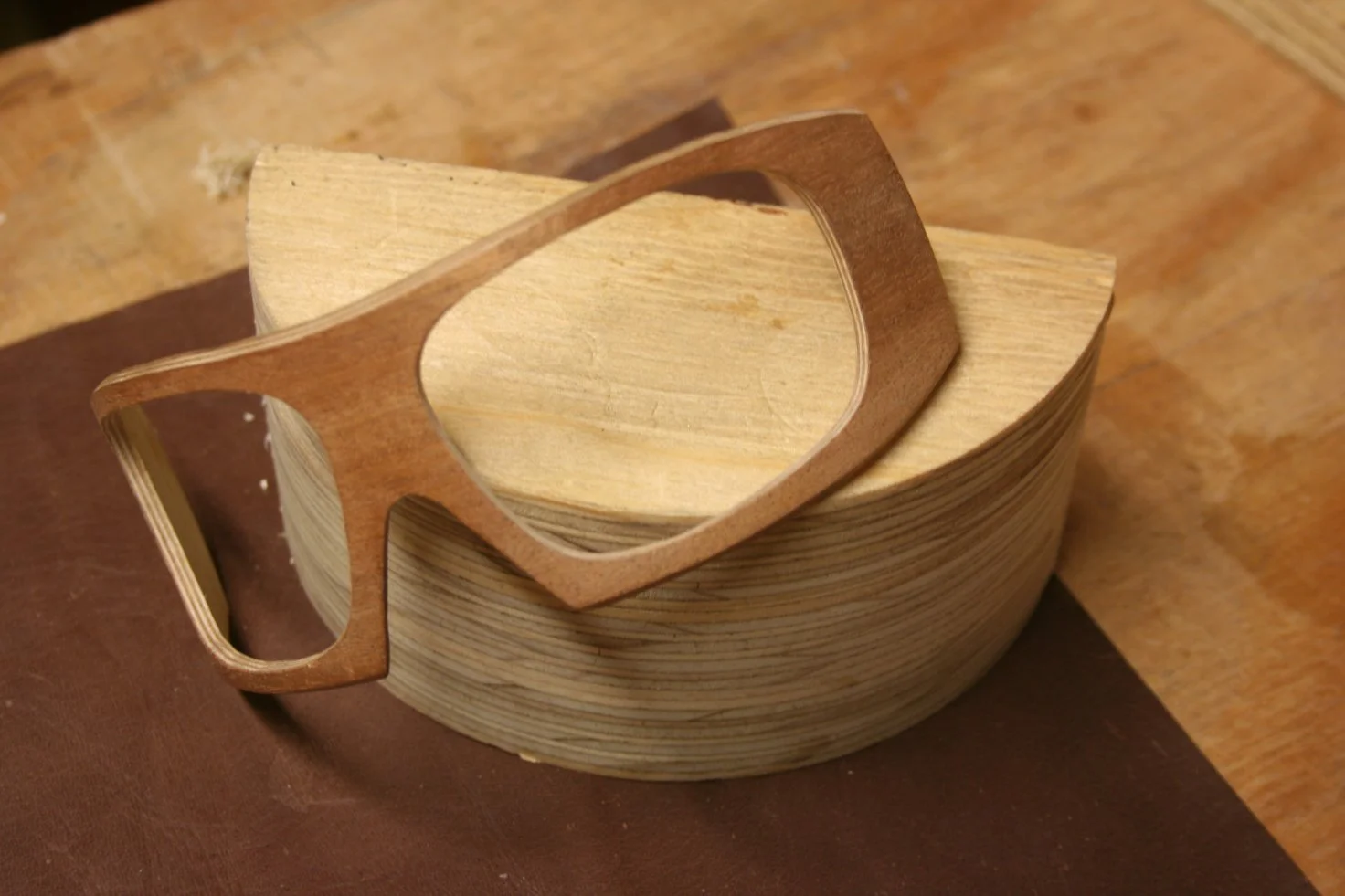 Stack of unfinished wooden bowls with a wooden sunglasses frame placed on top, on a wooden surface.