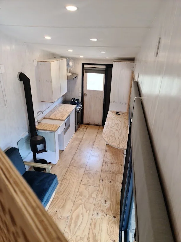 Paneling, built in cupboards and other storage compartments in the tiny house is finished in various shades of white with a clear coated and pinstriped floor.