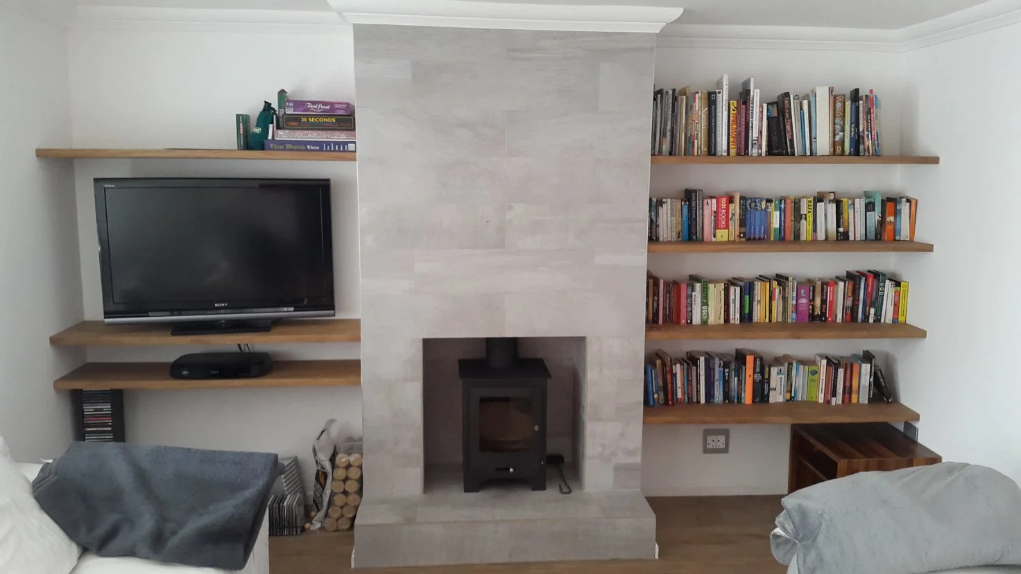 Living room with a fireplace, bookshelf, TV on a wall-mounted shelf, and a wood stove in the fireplace opening.