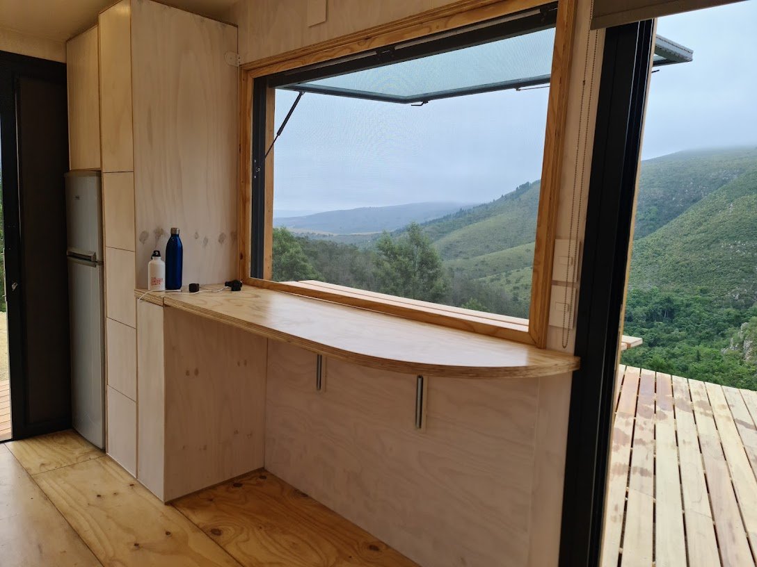 The staircase serves for loads of utility space and houses the laundry accessible from the outside of the CaveLet tiny house. The inside-out bar counter lives out onto a 50 square meter hardwood deck and flips down on the inside the tiny house for s