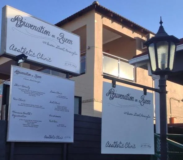 Exterior of a building with signs promoting a rejuvenation and aesthetic clinic, with a decorative street lamp nearby, under clear blue sky.
