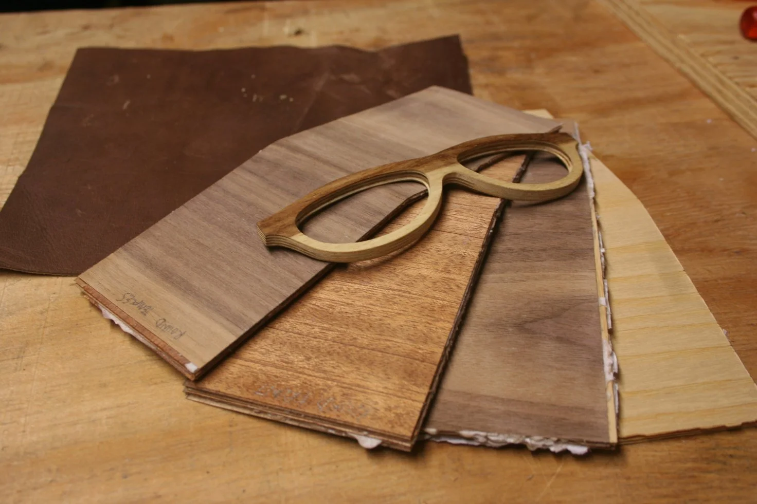 Various samples of wood veneer and a pair of glasses-shaped wooden cutouts on a worktable.