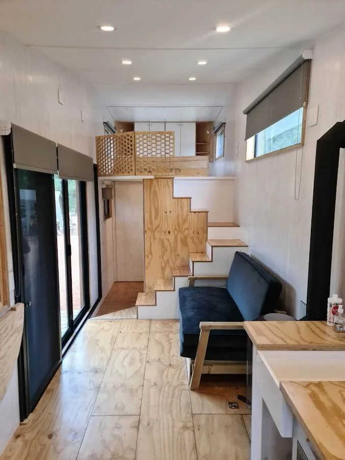 Paneling, built in cupboards and other storage compartments in the tiny house is finished in various shades of white with a clear coated and pinstriped floor.