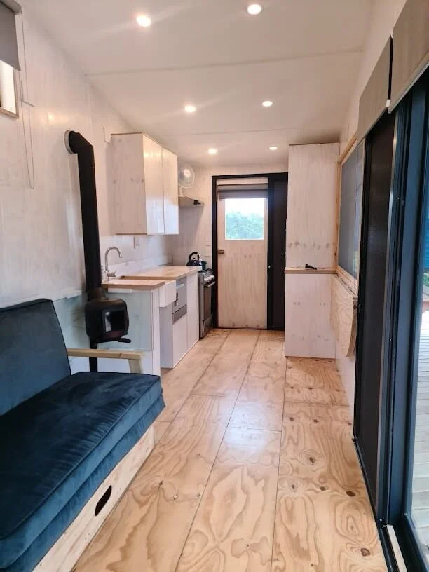 Paneling, built in cupboards and other storage compartments in the tiny house is finished in various shades of white with a clear coated and pinstriped floor.