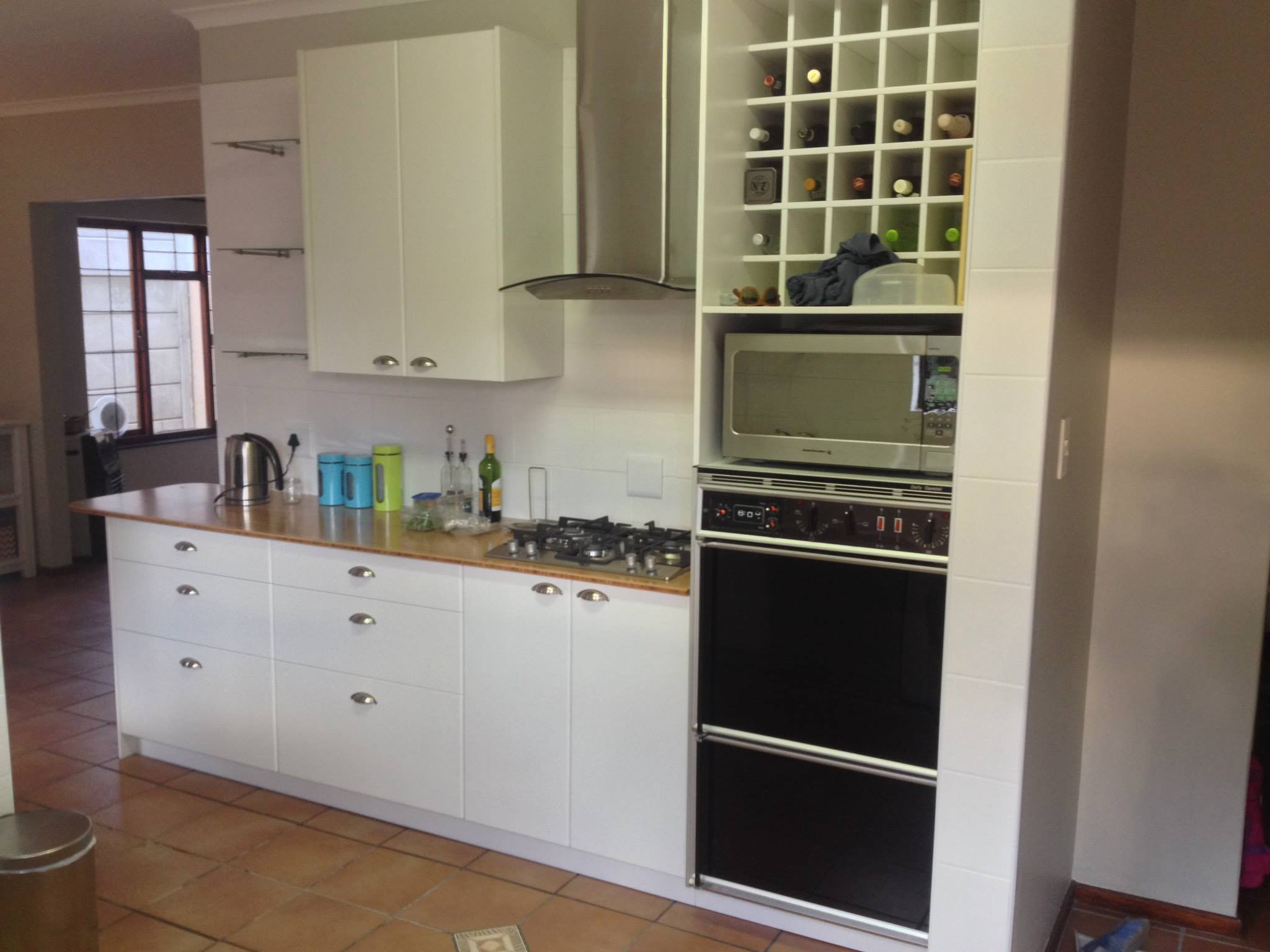 Kitchen with white cabinets, a stovetop, a microwave, a wine rack, and various kitchen bottles and utensils on the countertop.