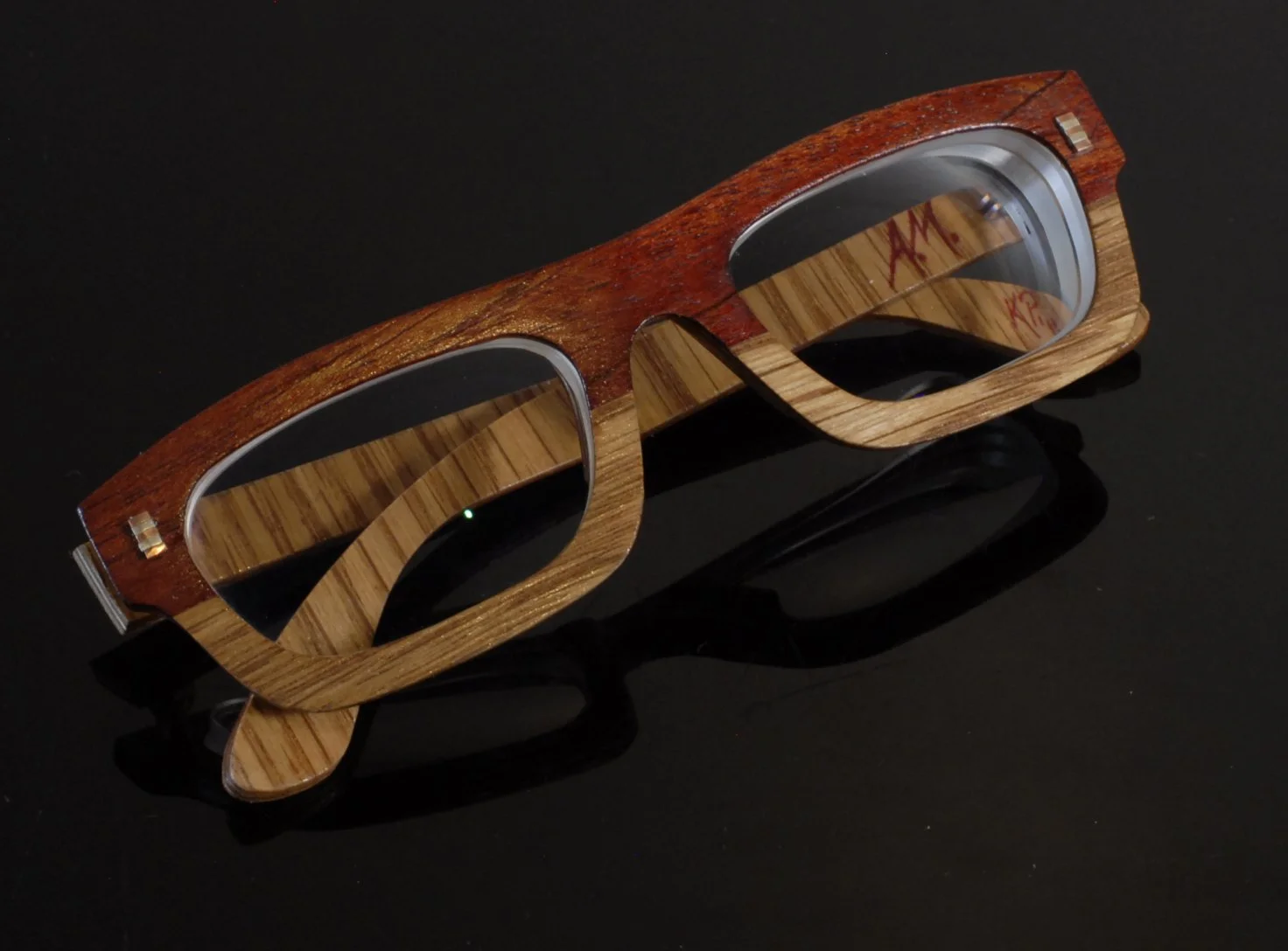 Wooden and metal sunglasses on a black surface.